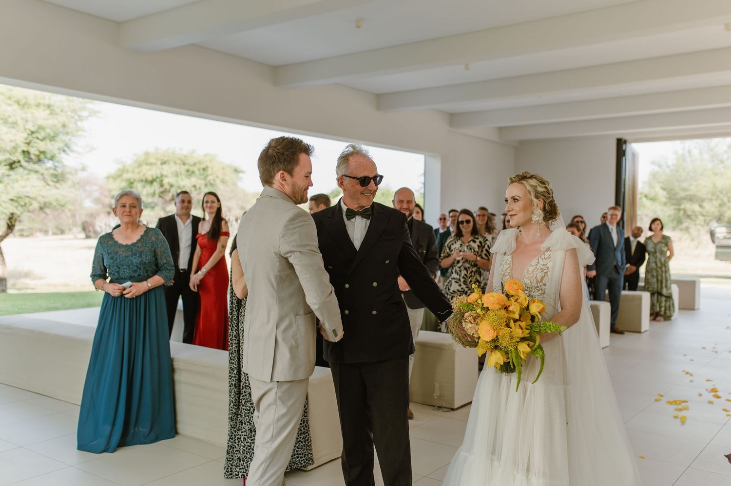 Wedding ceremony with guests gathered in bright indoor space featuring yellow sunflower bouquets.