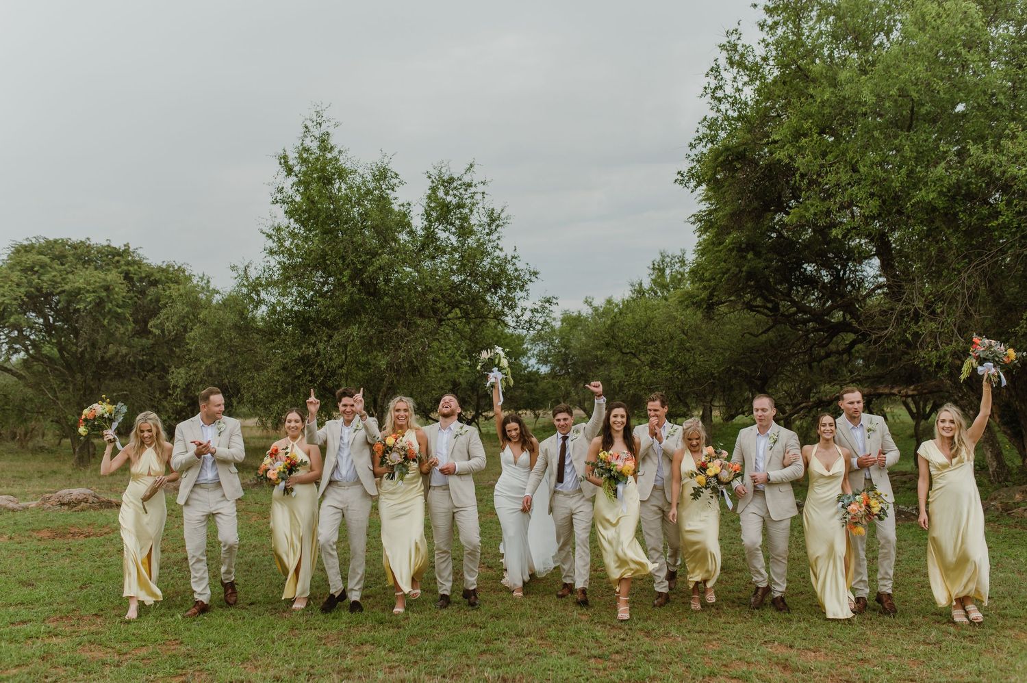 Wedding party runs joyfully across a green field in coordinated white and yellow outfits.