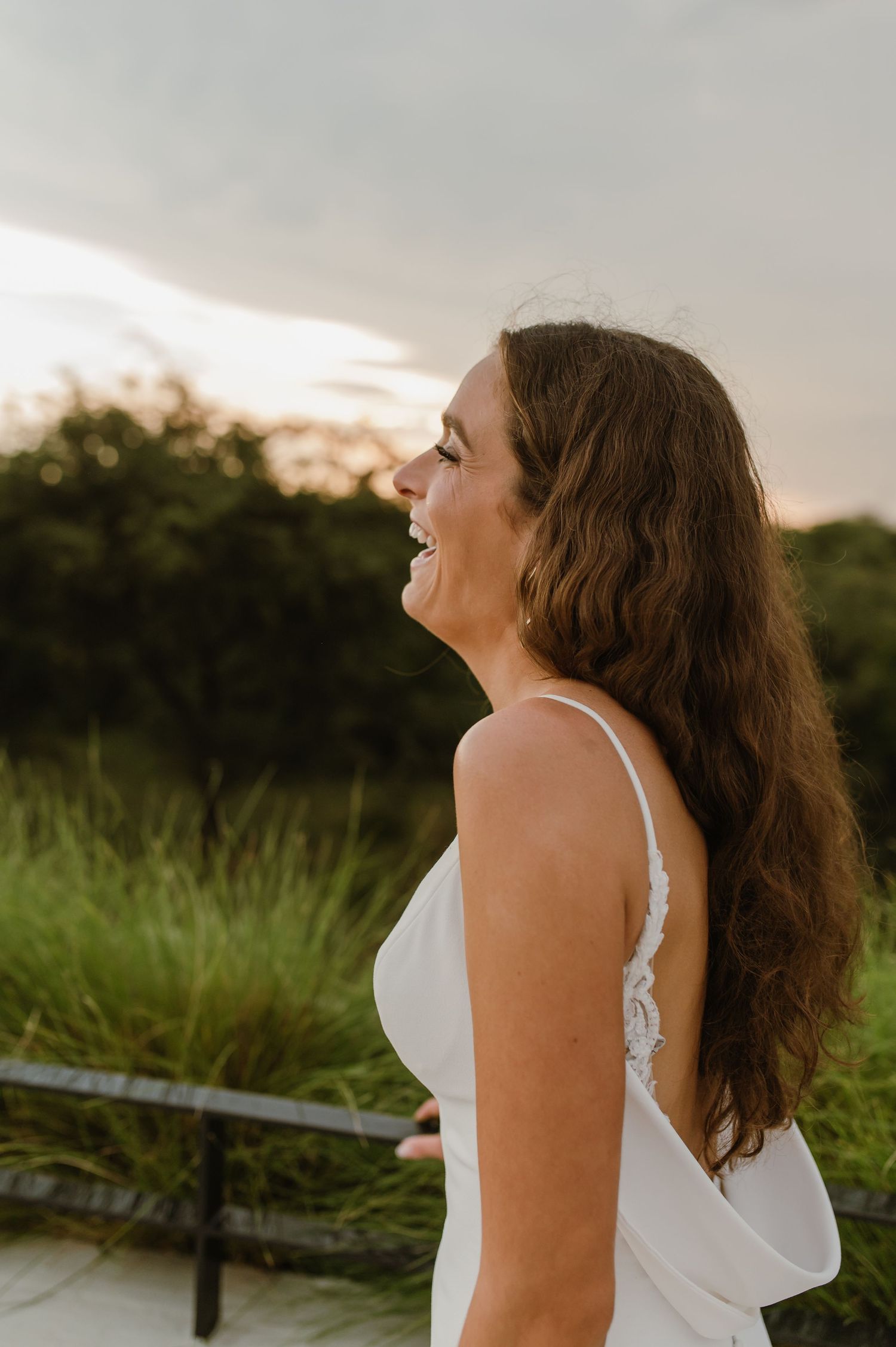 Candid shot of bride laughing with flowing hair at sunset.