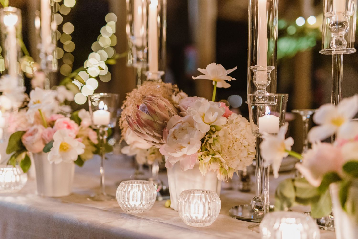 Delicate floral centerpieces and candlelight create romantic ambiance at wedding reception tables.