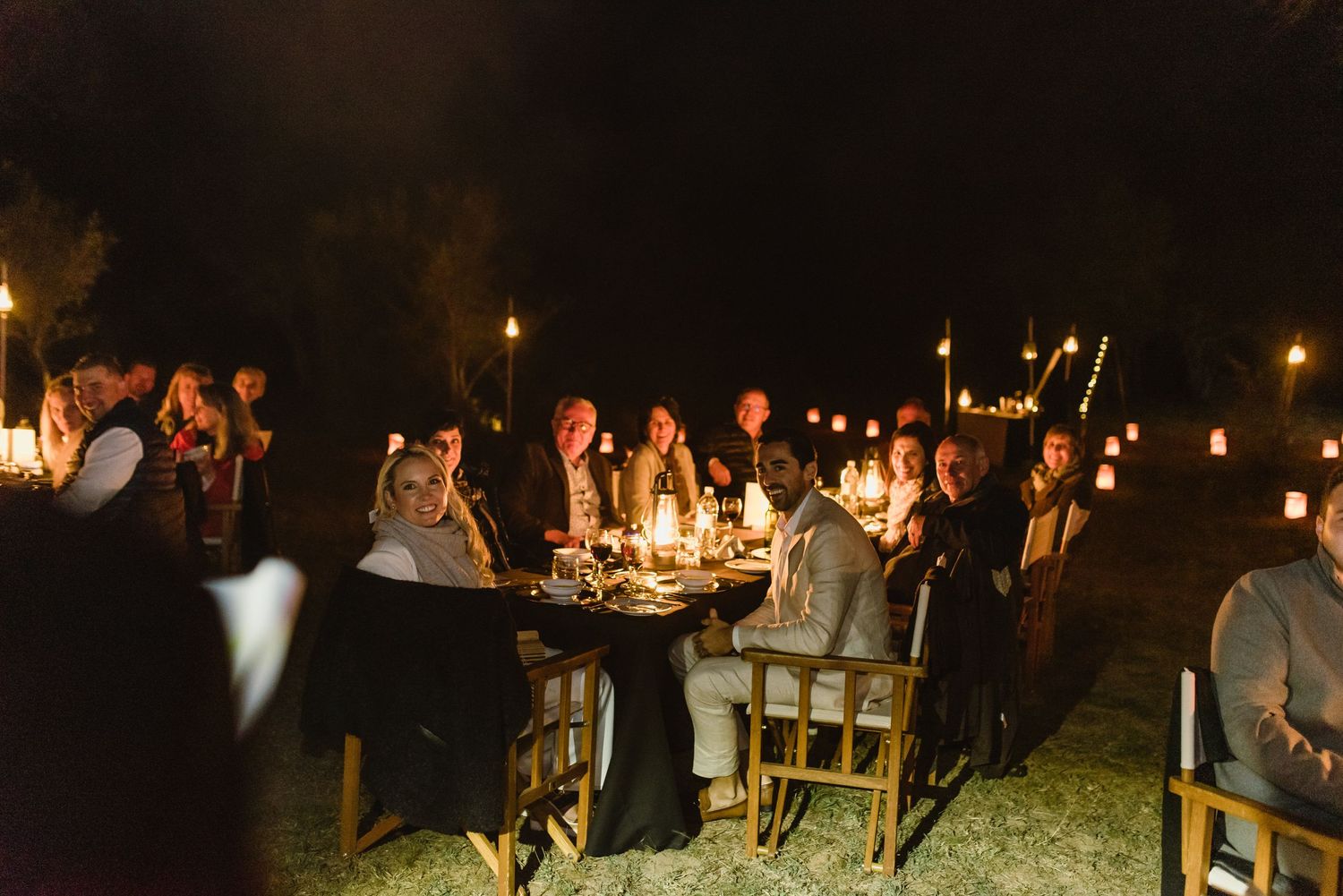 Evening outdoor party scene with candlelit tables and festive lighting.
