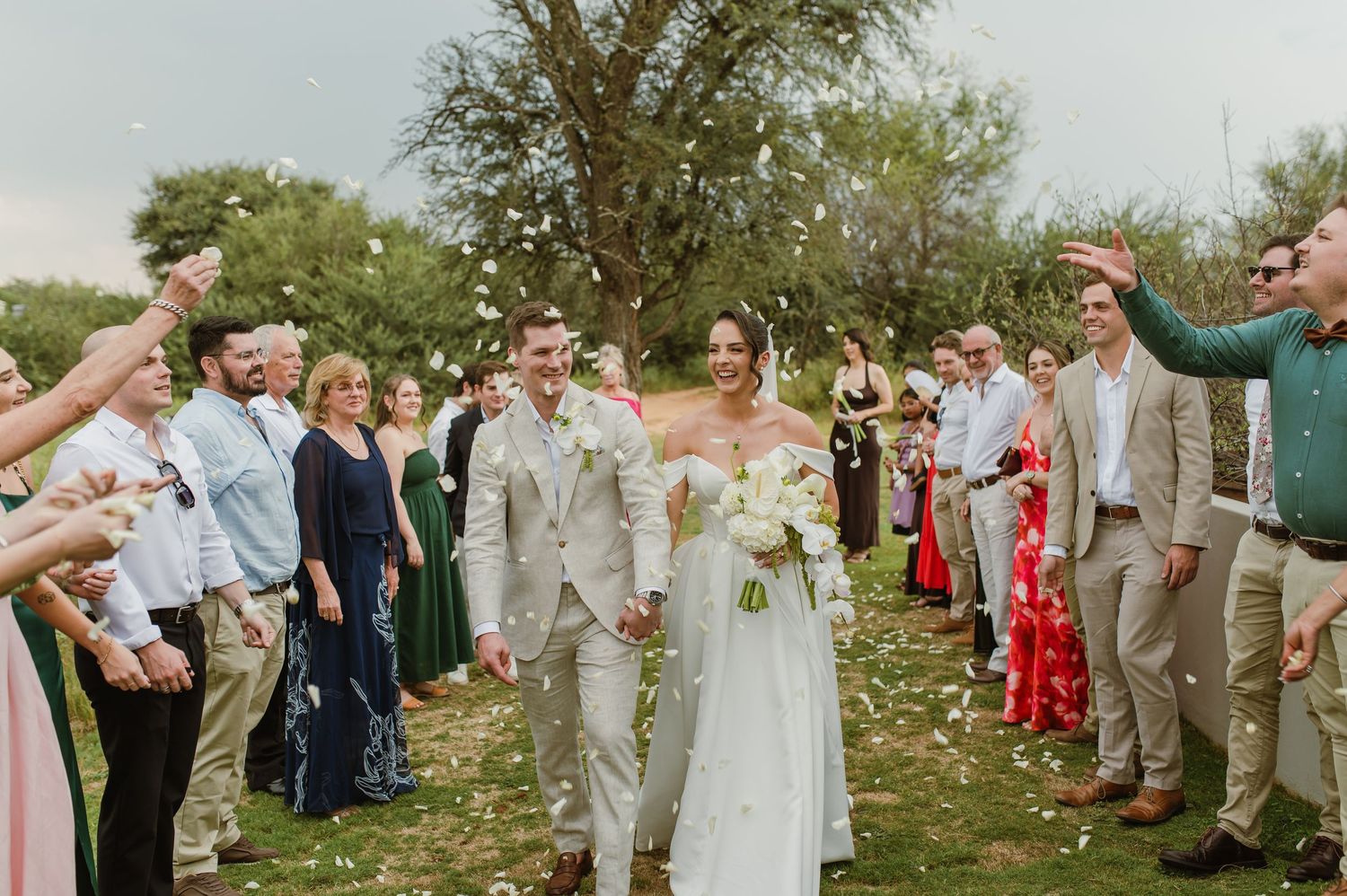 Wedding guests toss flower petals at the newlyweds during an outdoor garden celebration.