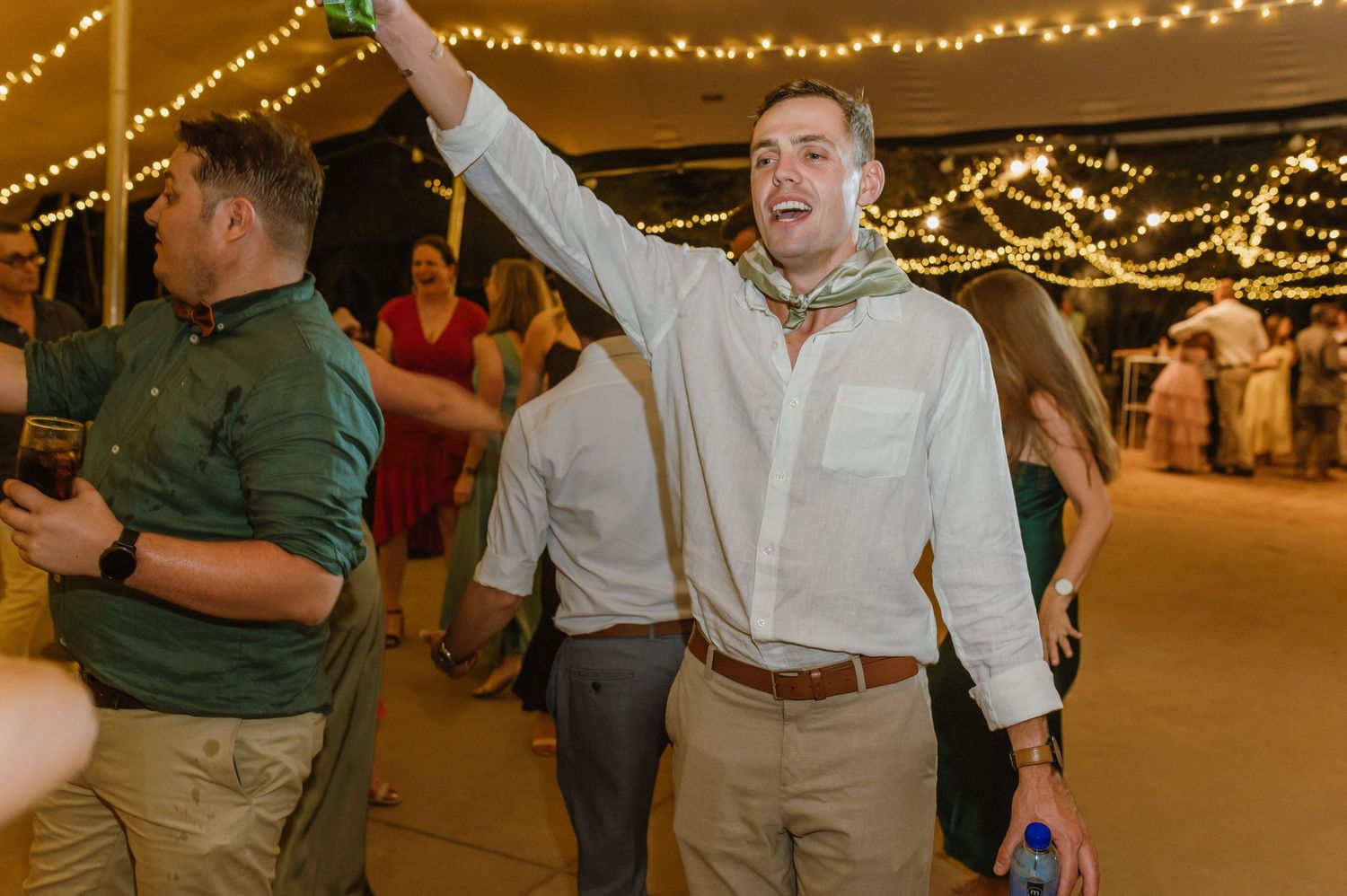 Energetic dance party at a wedding reception with guests celebrating under string lights.
