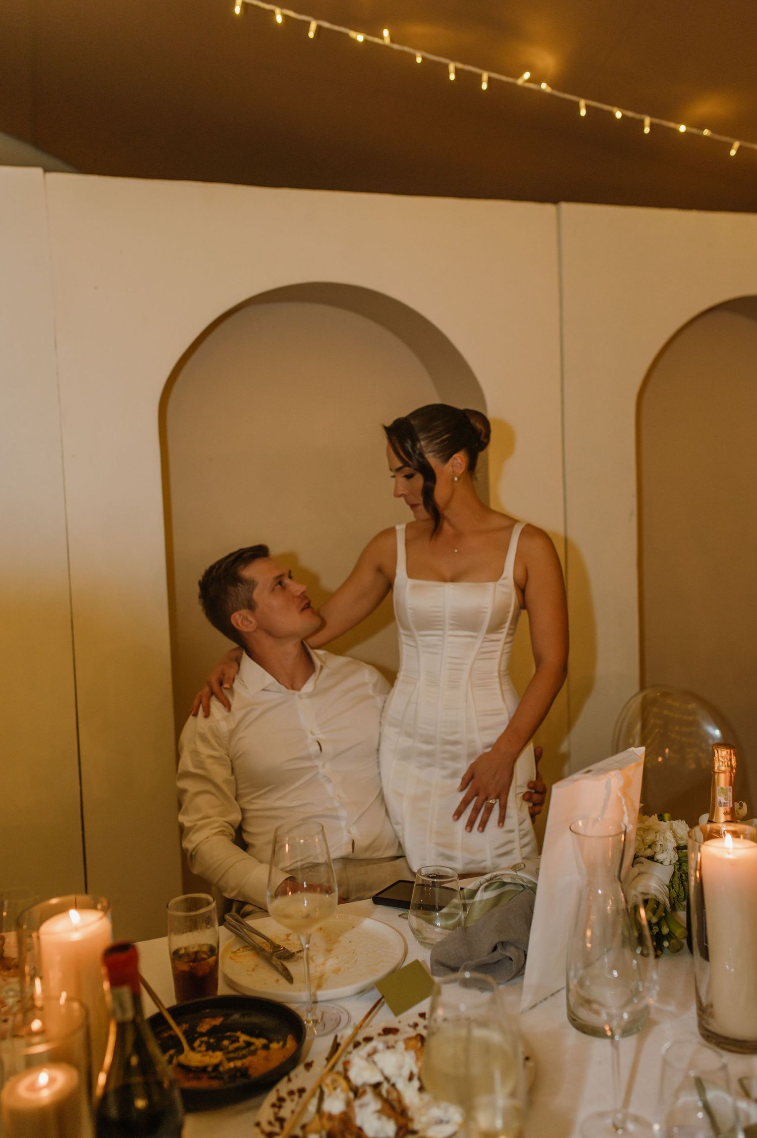 Candlelit wedding reception table with elegant place settings and string lights overhead.