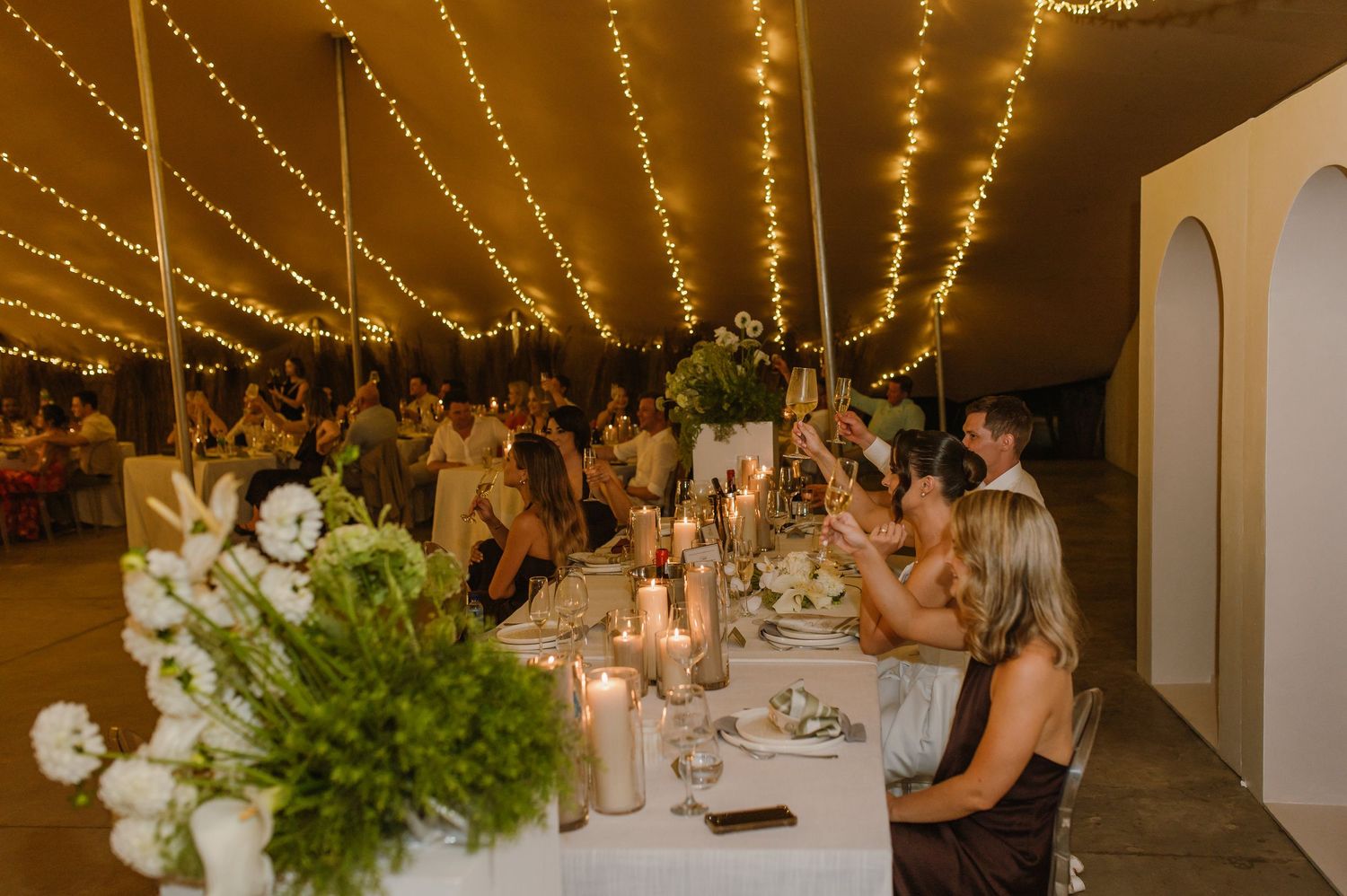Wedding reception venue decorated with twinkling string lights and elegant white floral centerpieces.