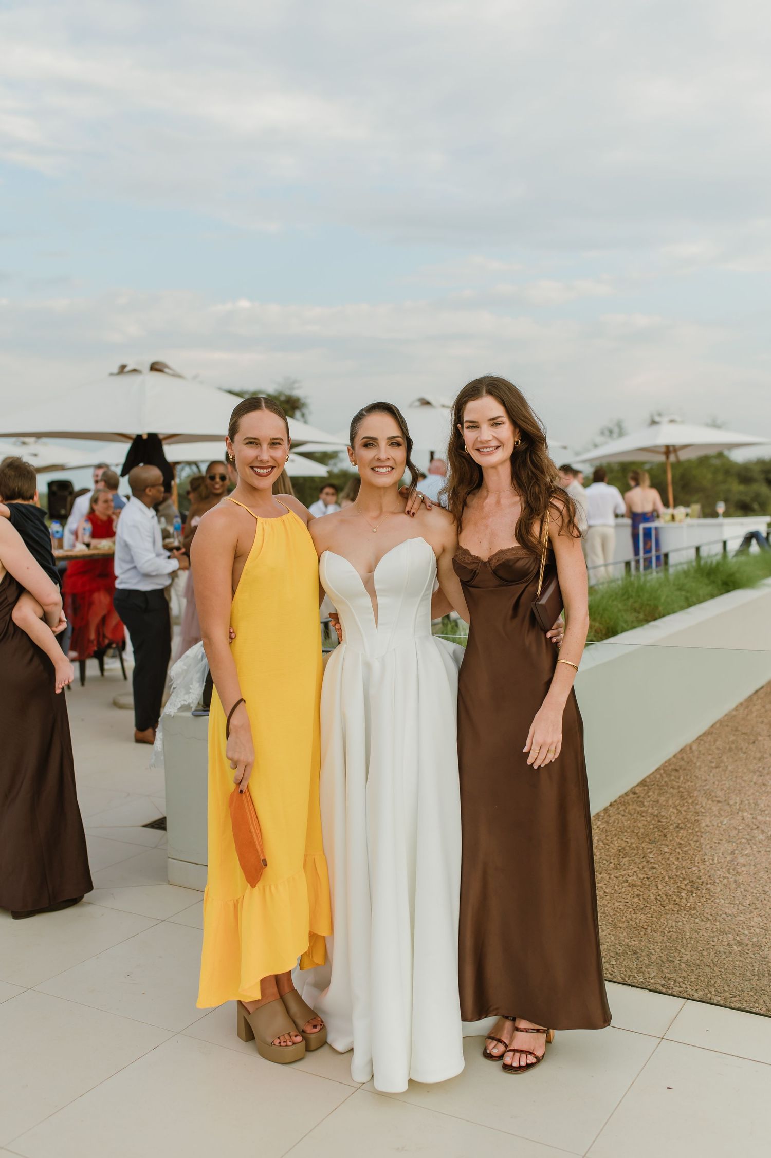 Wedding party members in yellow and brown dresses pose together on an outdoor terrace.