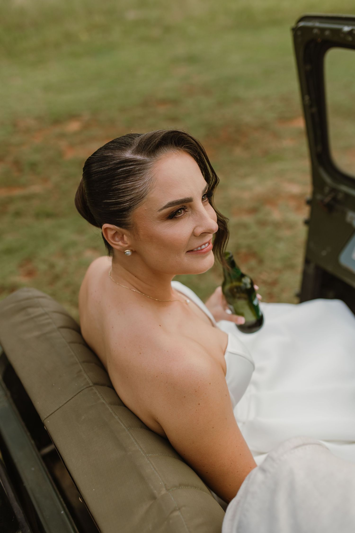 A wedding dress elegantly draped over the side of a classic military vehicle in a natural outdoor setting.