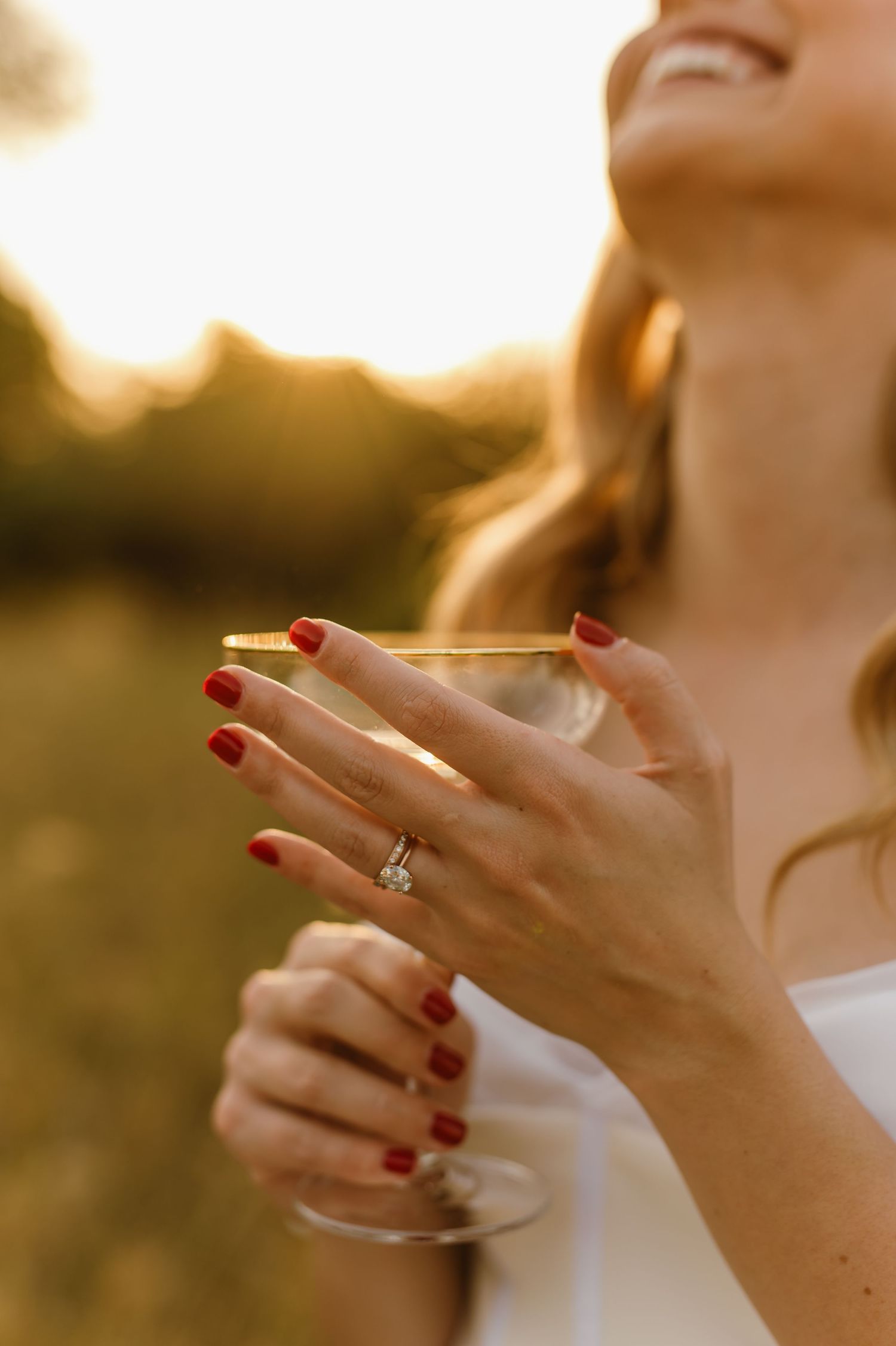 Close-up of hands with red nail polish and engagement ring in golden sunset light.