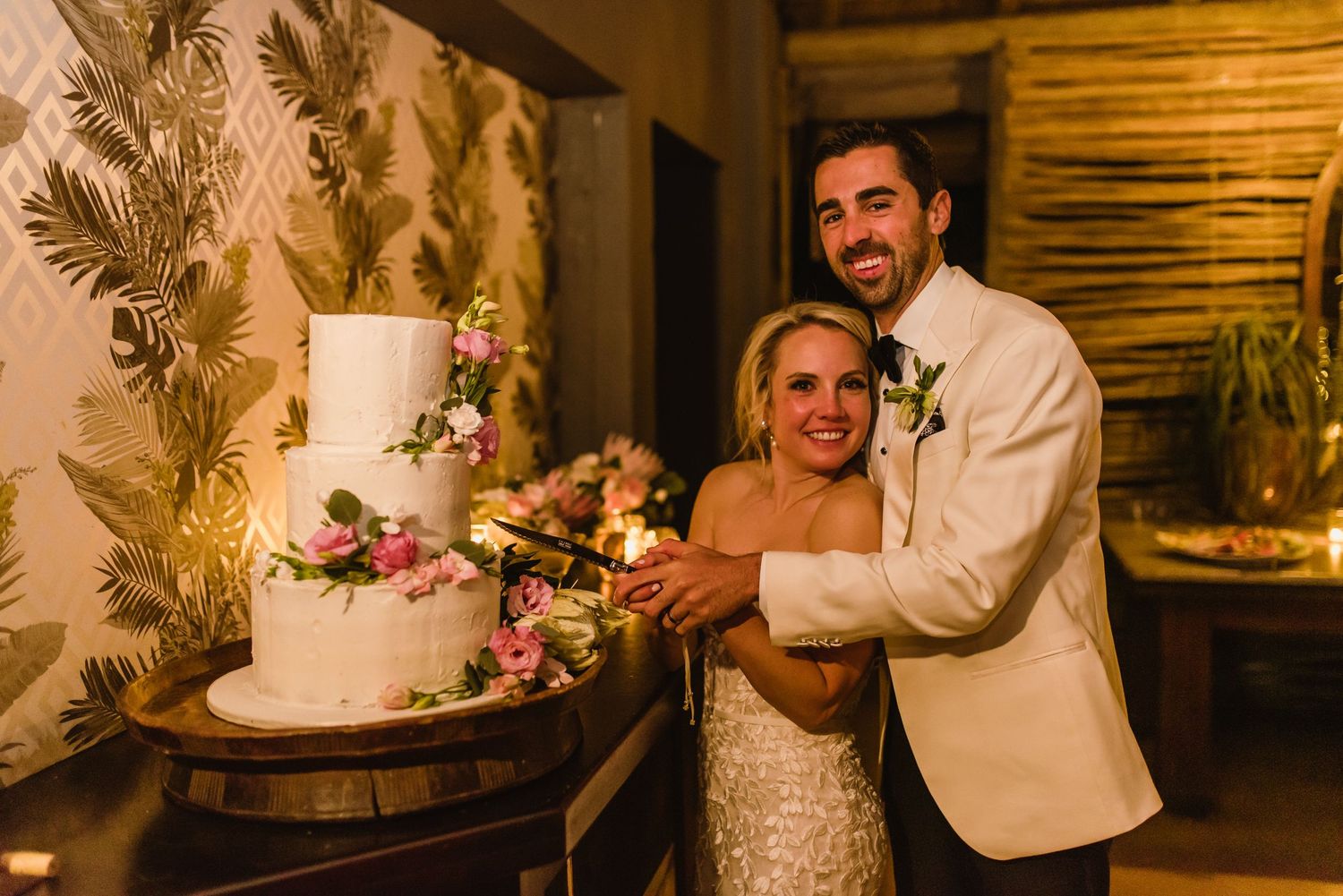 Wedding cake cutting moment captured in warm lighting with elegant floral decorations.