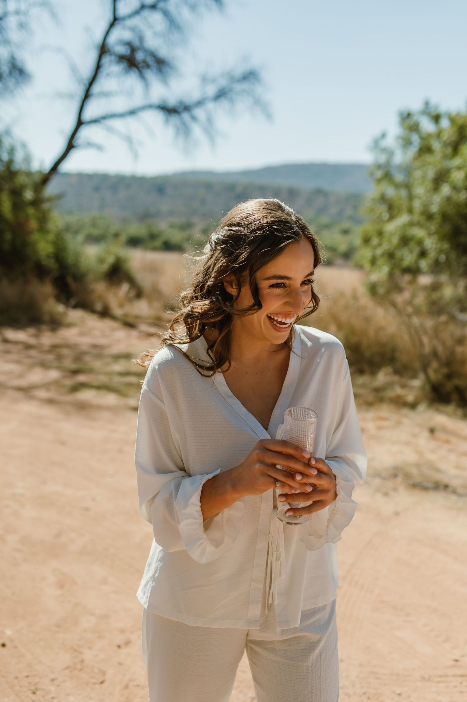 Someone in a white dress laughs joyfully while standing in a desert landscape.