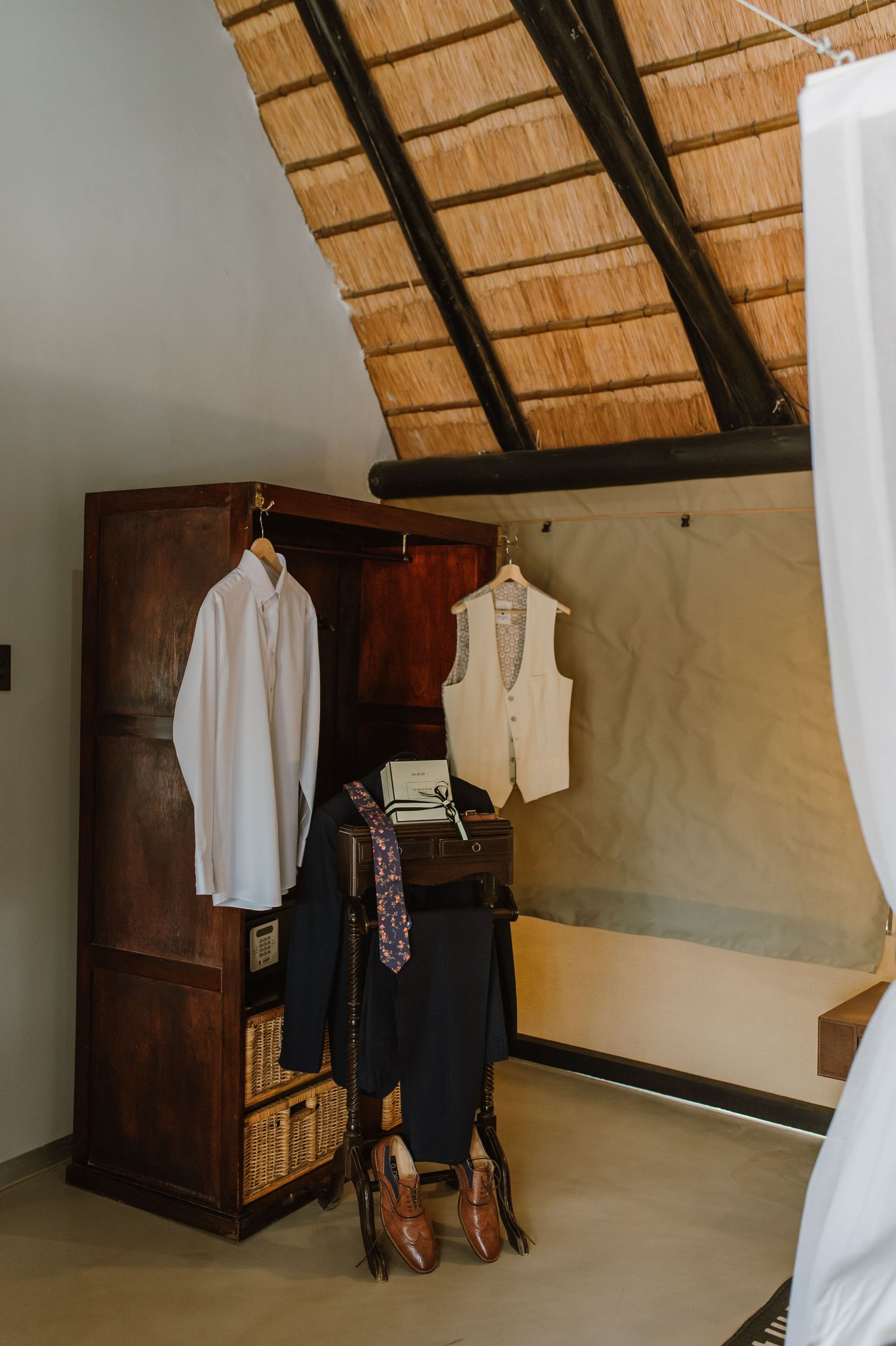 Interior view of a thatched roof room with white walls and hanging formal clothing.