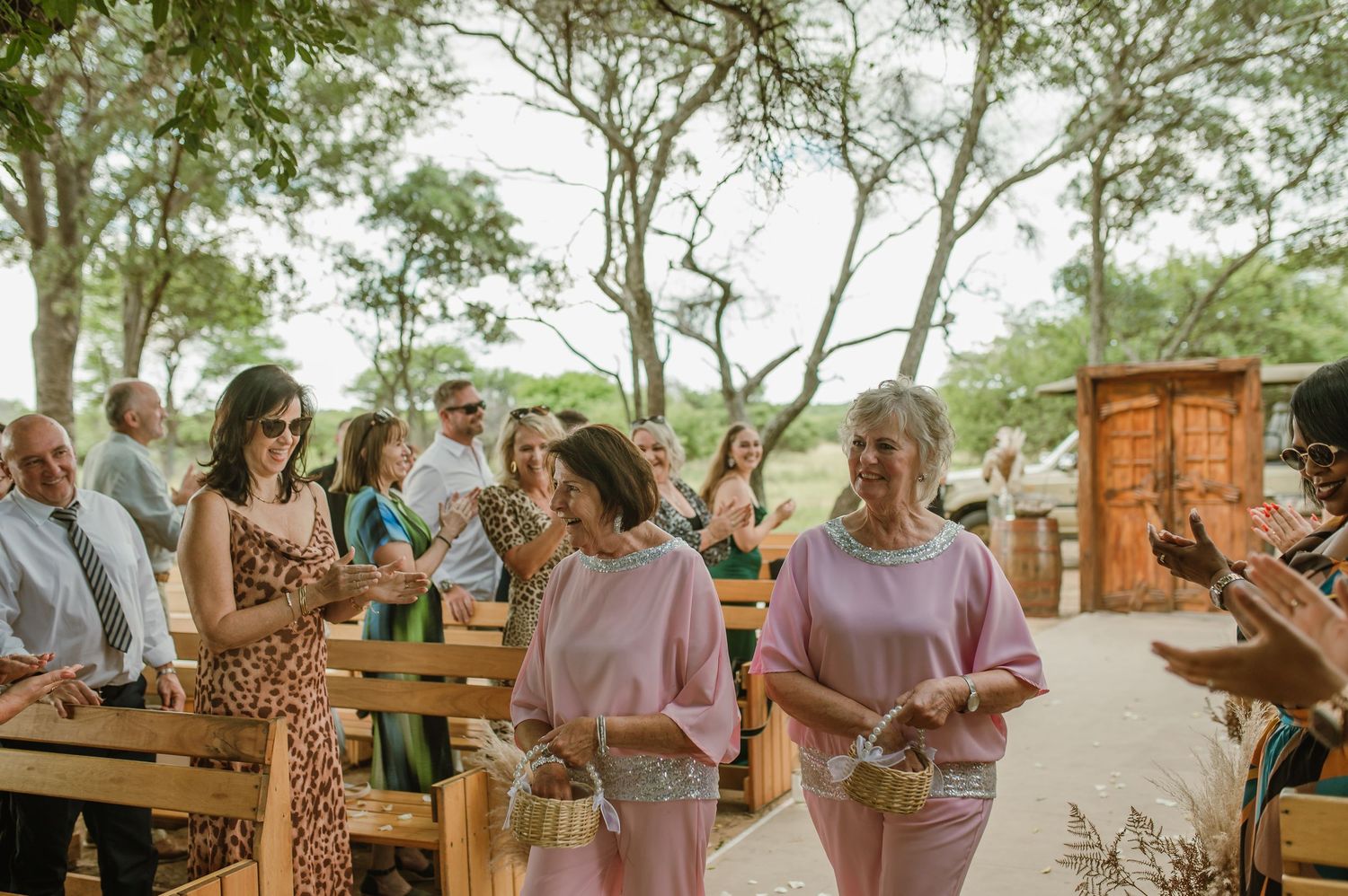 Wedding guests in colorful attire walking through an outdoor venue with wooden benches.