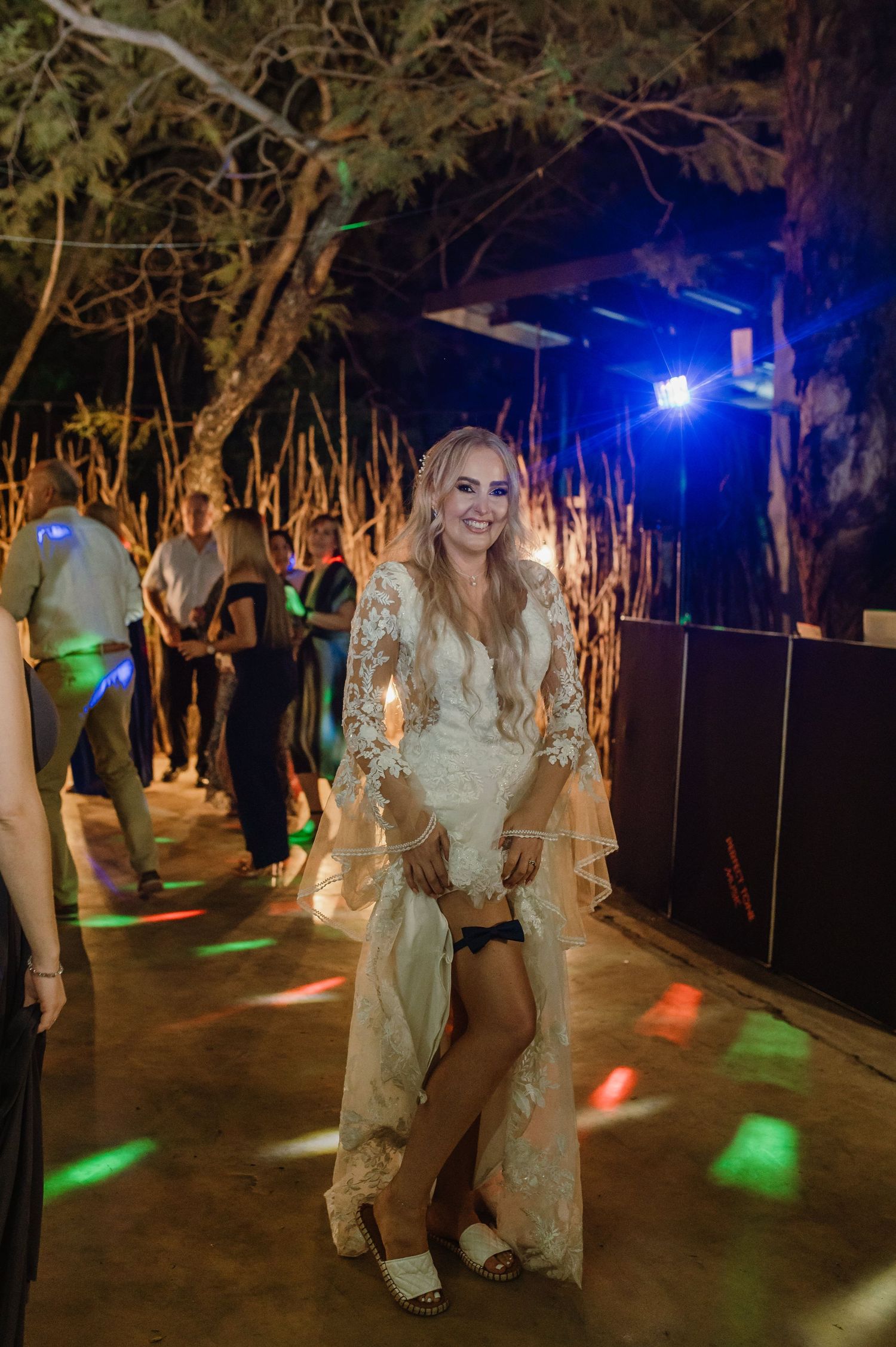 Outdoor wedding reception dance floor with colorful lighting and natural tree backdrop.