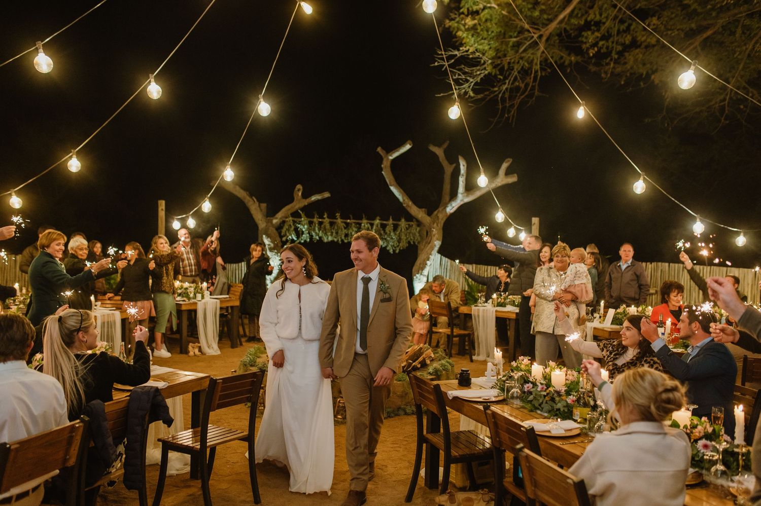 An outdoor wedding reception venue at night illuminated by warm string lights and lanterns.