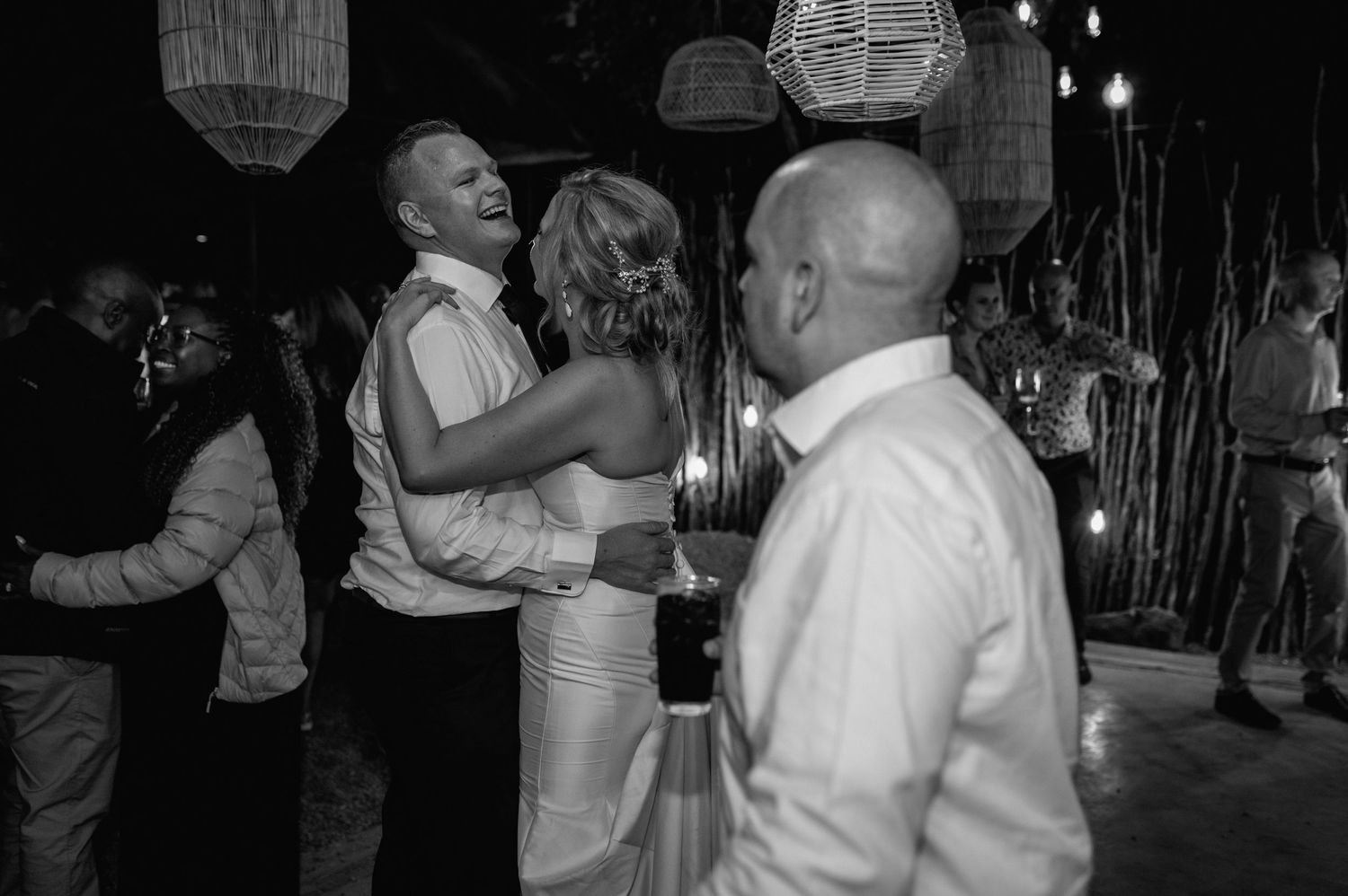 Couples dancing together at a dimly lit wedding reception with string lights overhead.