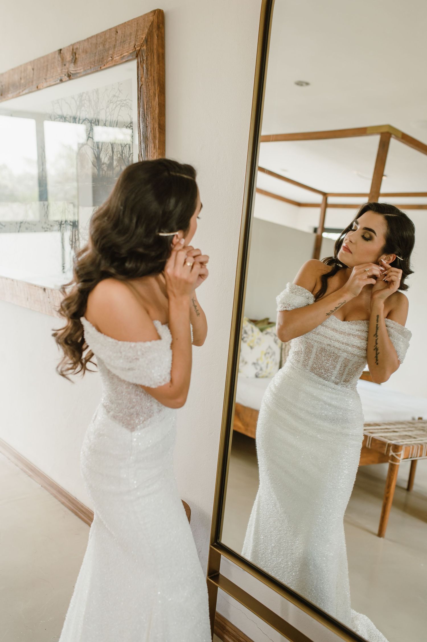Someone in a white dress looking at their reflection in a rustic framed mirror.