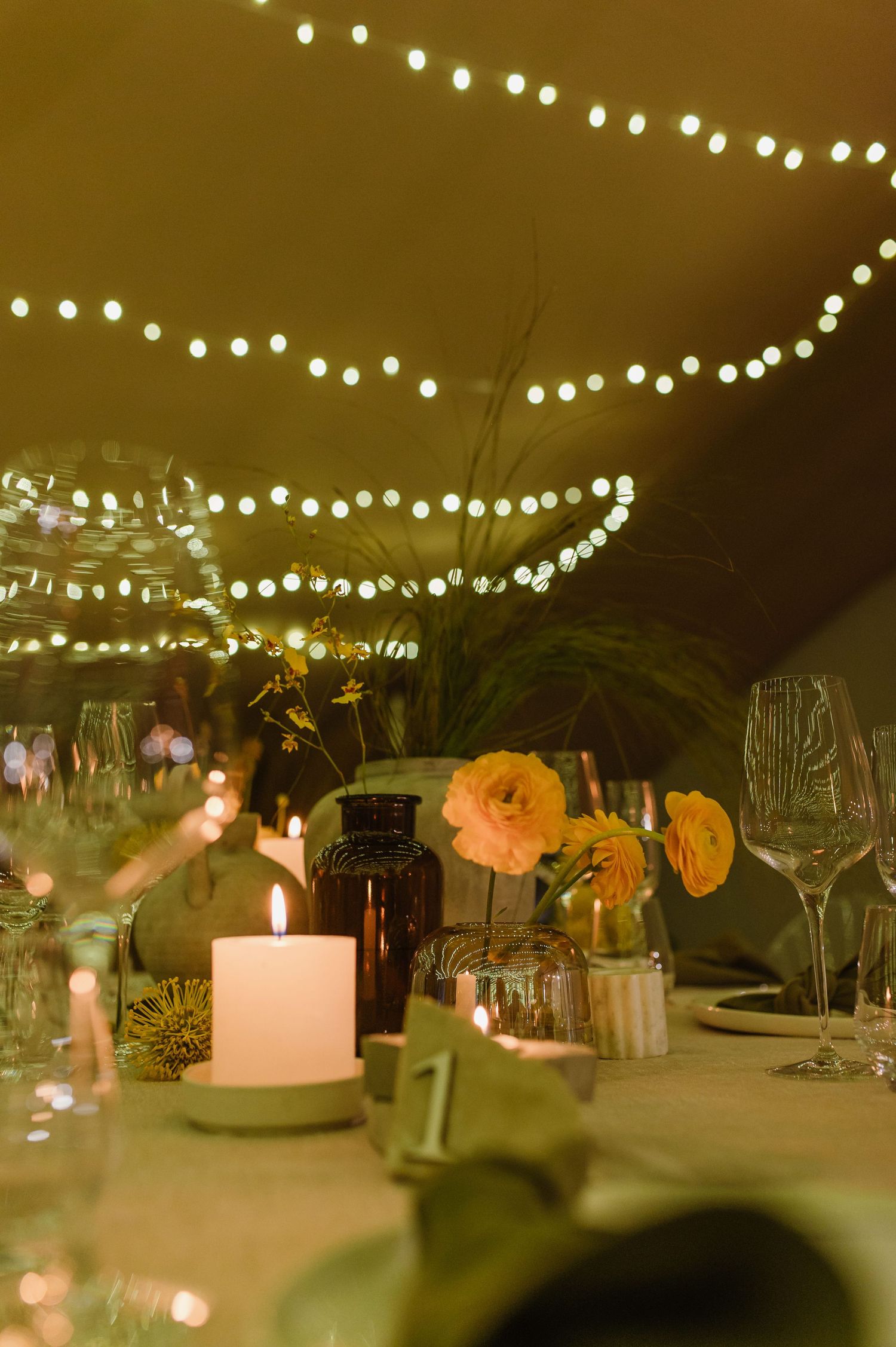 Romantic table setting with glowing candles and string lights creating warm ambiance at evening event.