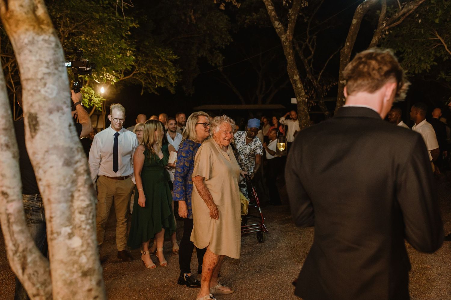 Guests mingling at an elegant outdoor evening reception under trees.