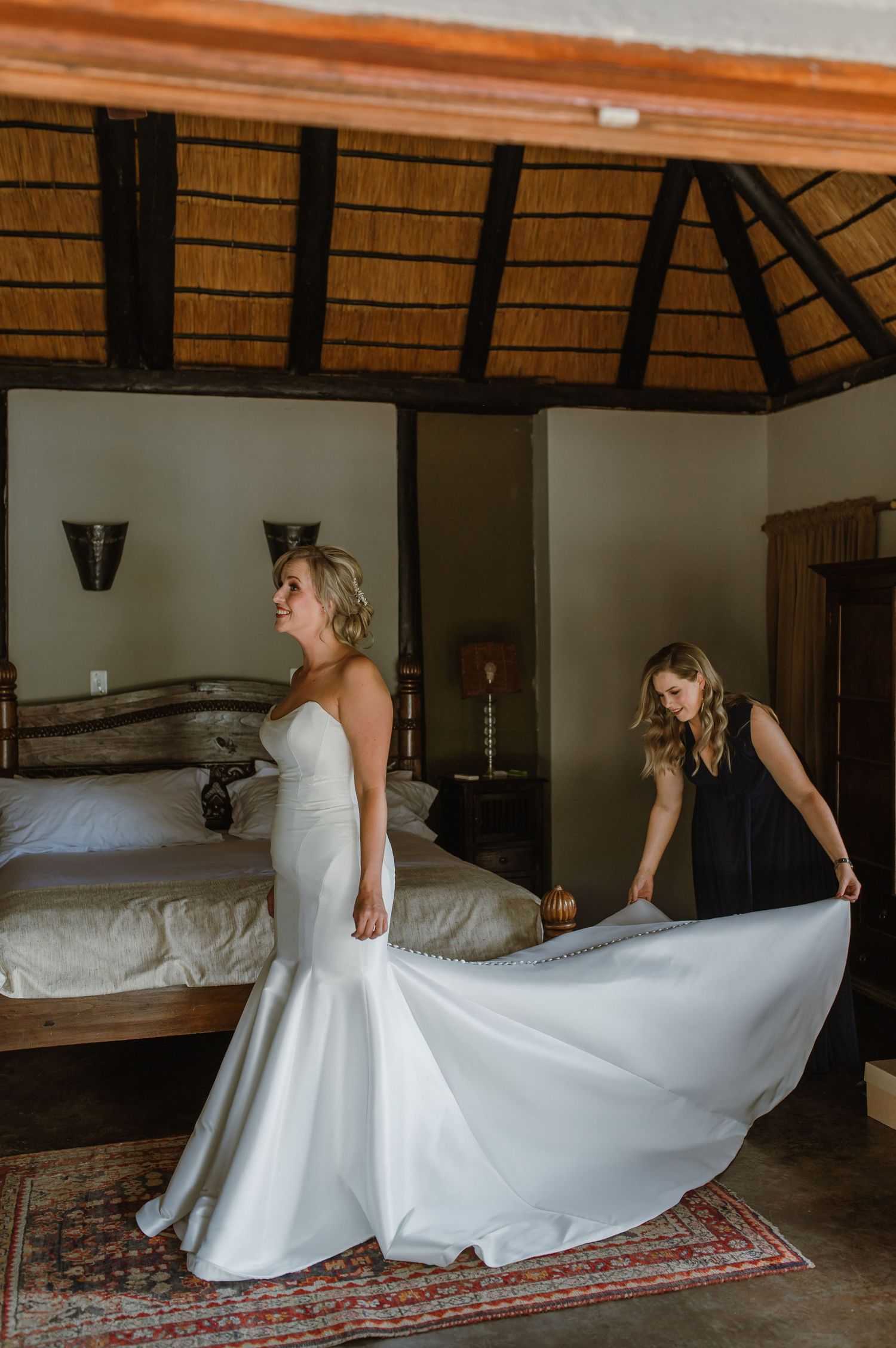 White wedding dress twirling on ornate rug in rustic room with thatched ceiling.