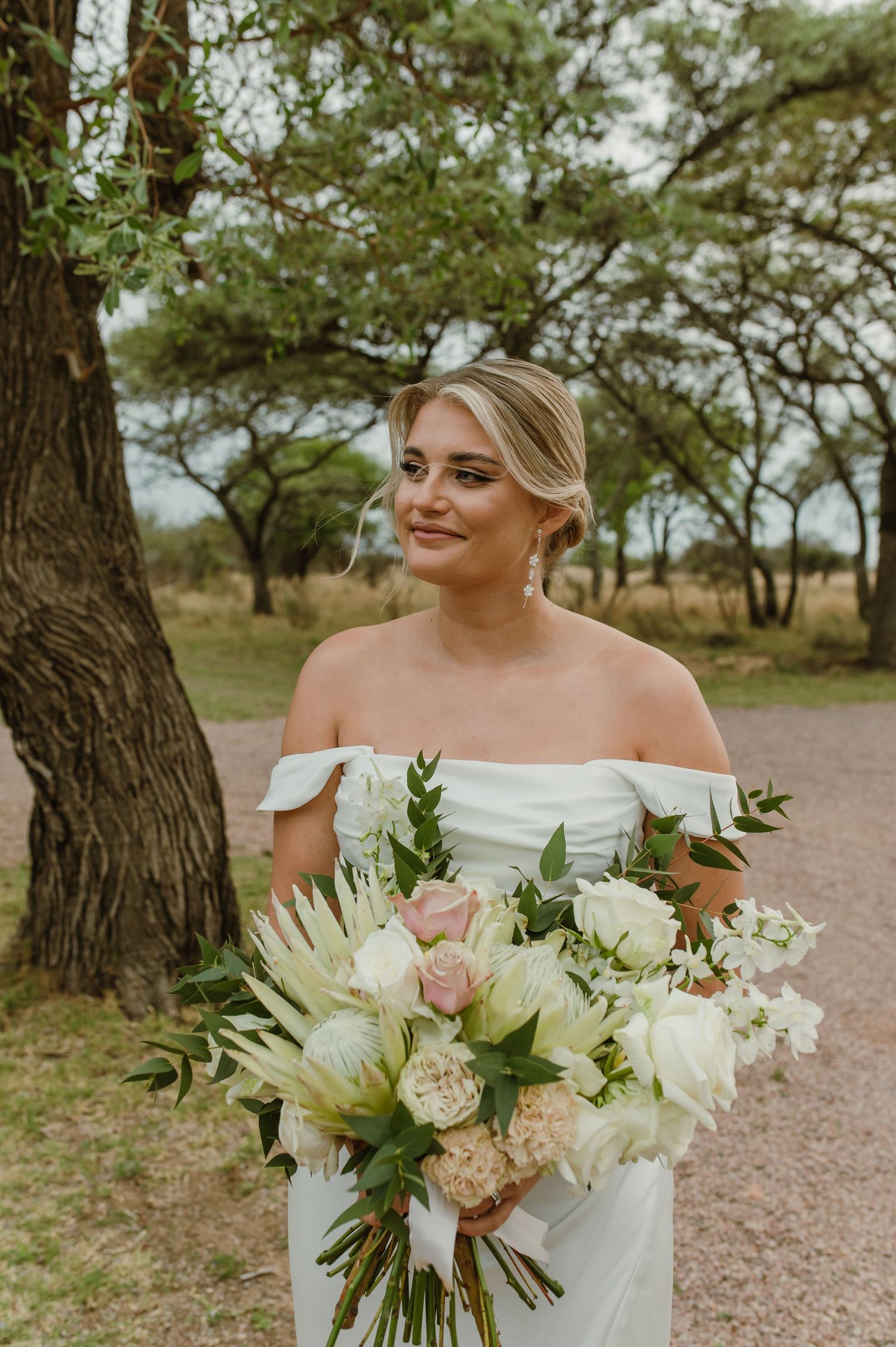 Beautiful white and cream wedding bouquet with roses and greenery against a natural outdoor backdrop.