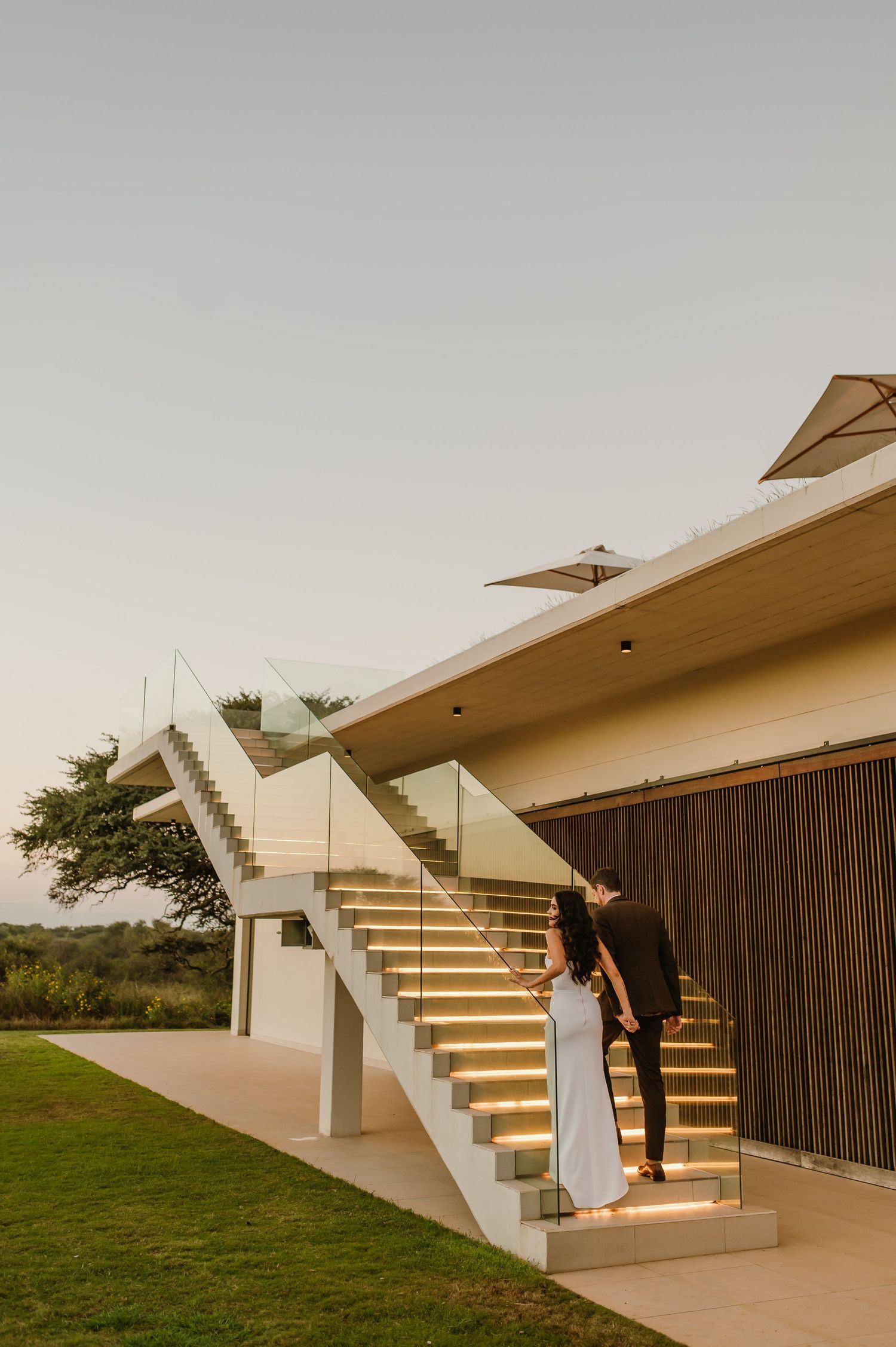A couple poses on modern white architectural stairs with LED lighting.