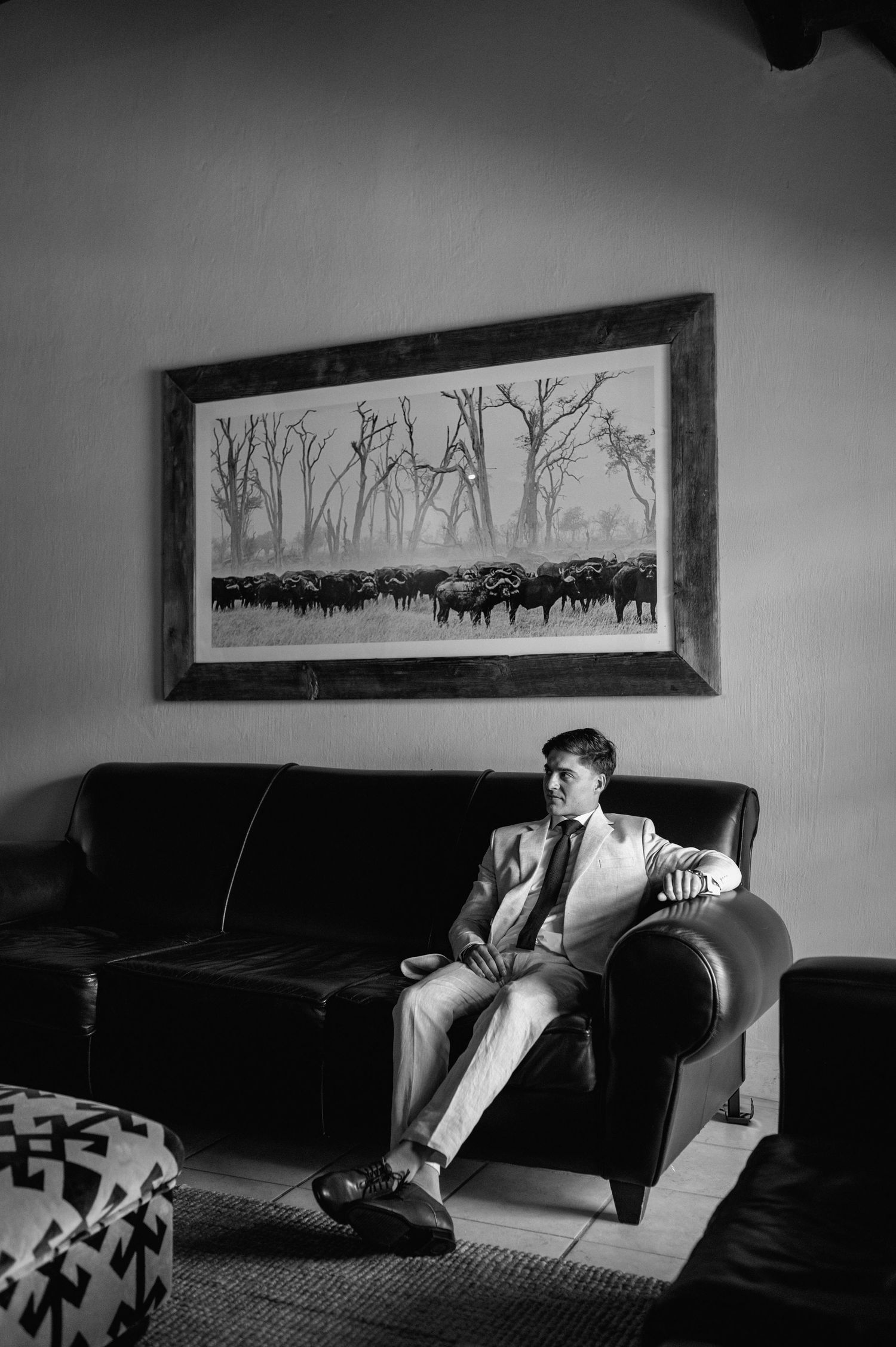 Black and white series showing someone relaxing on a dark couch under landscape artwork.