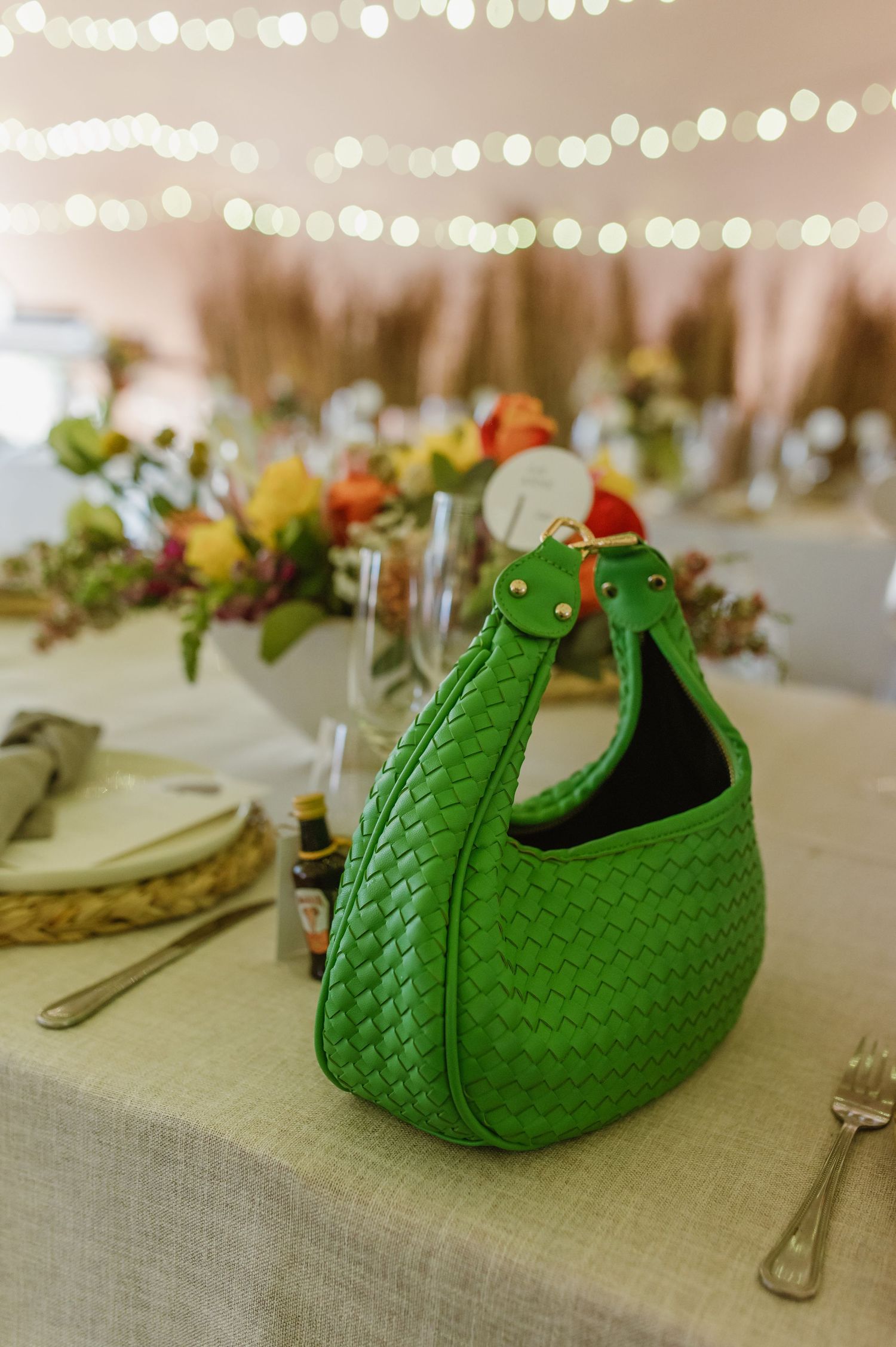 Green decorative purse displayed on table setting with string lights overhead.