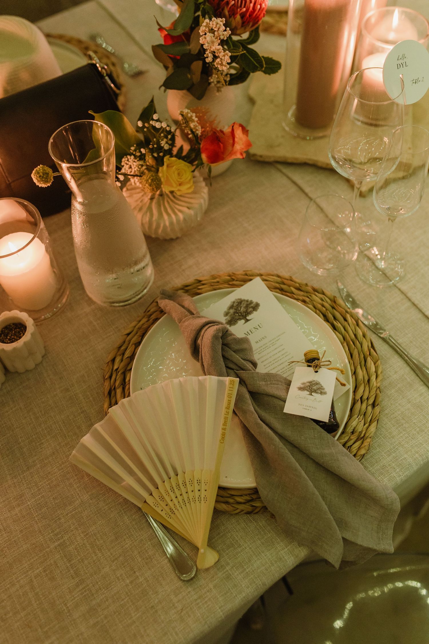 Wedding table decor featuring decorative fans, woven placemats, and floral arrangements.