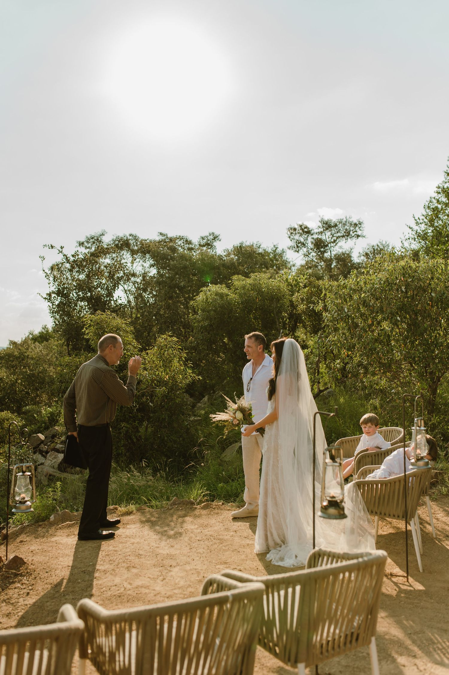 Outdoor wedding ceremony with bride and groom standing before officiant surrounded by lush greenery.
