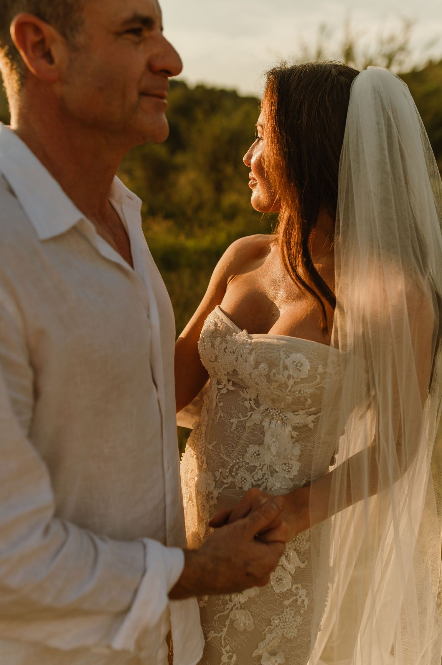 Couple embraces in warm sunset light, bride in lace gown with veil smiles at groom.