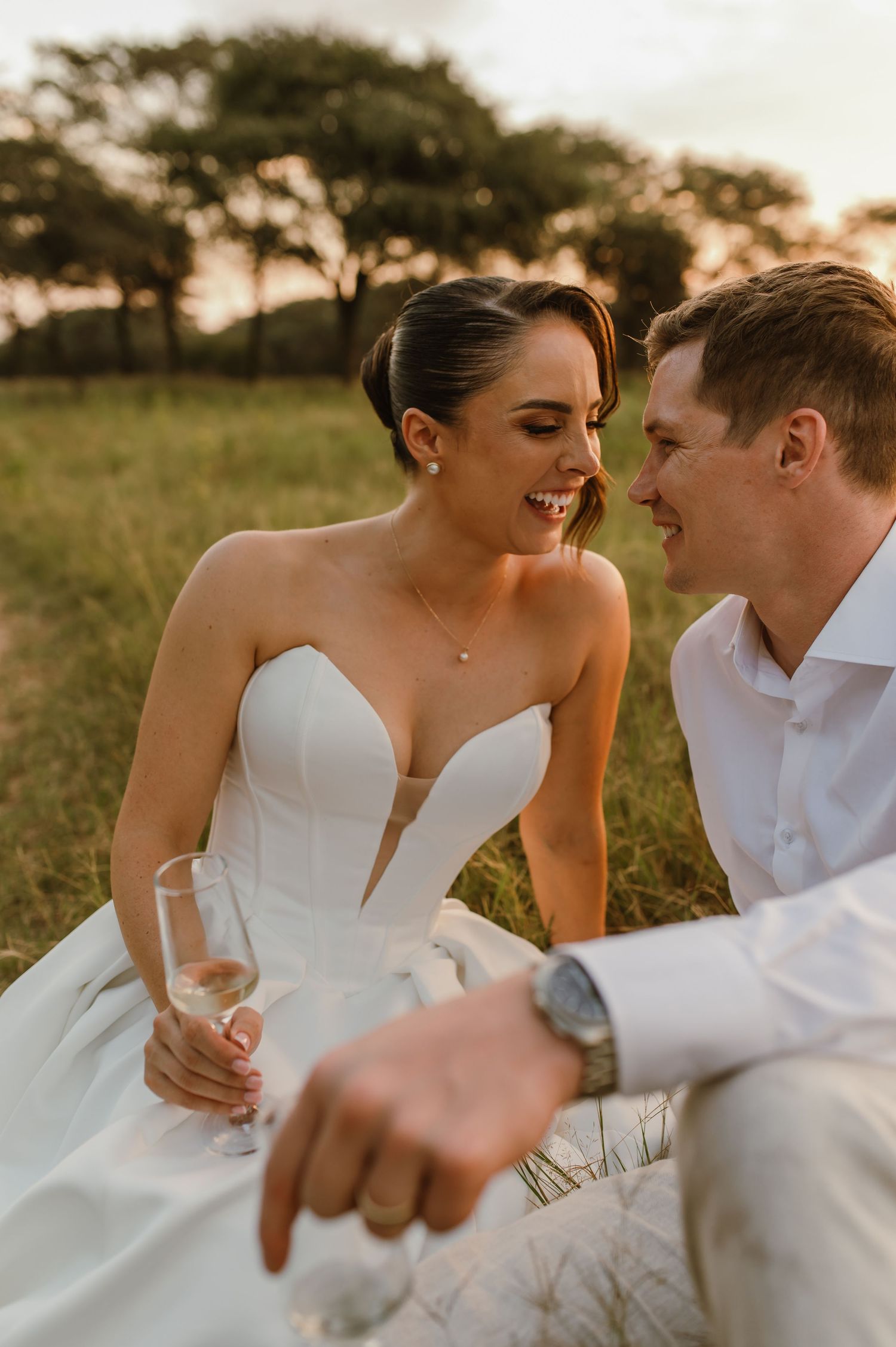 A romantic couple shares an intimate moment in a sunlit field while holding champagne glasses at sunset.