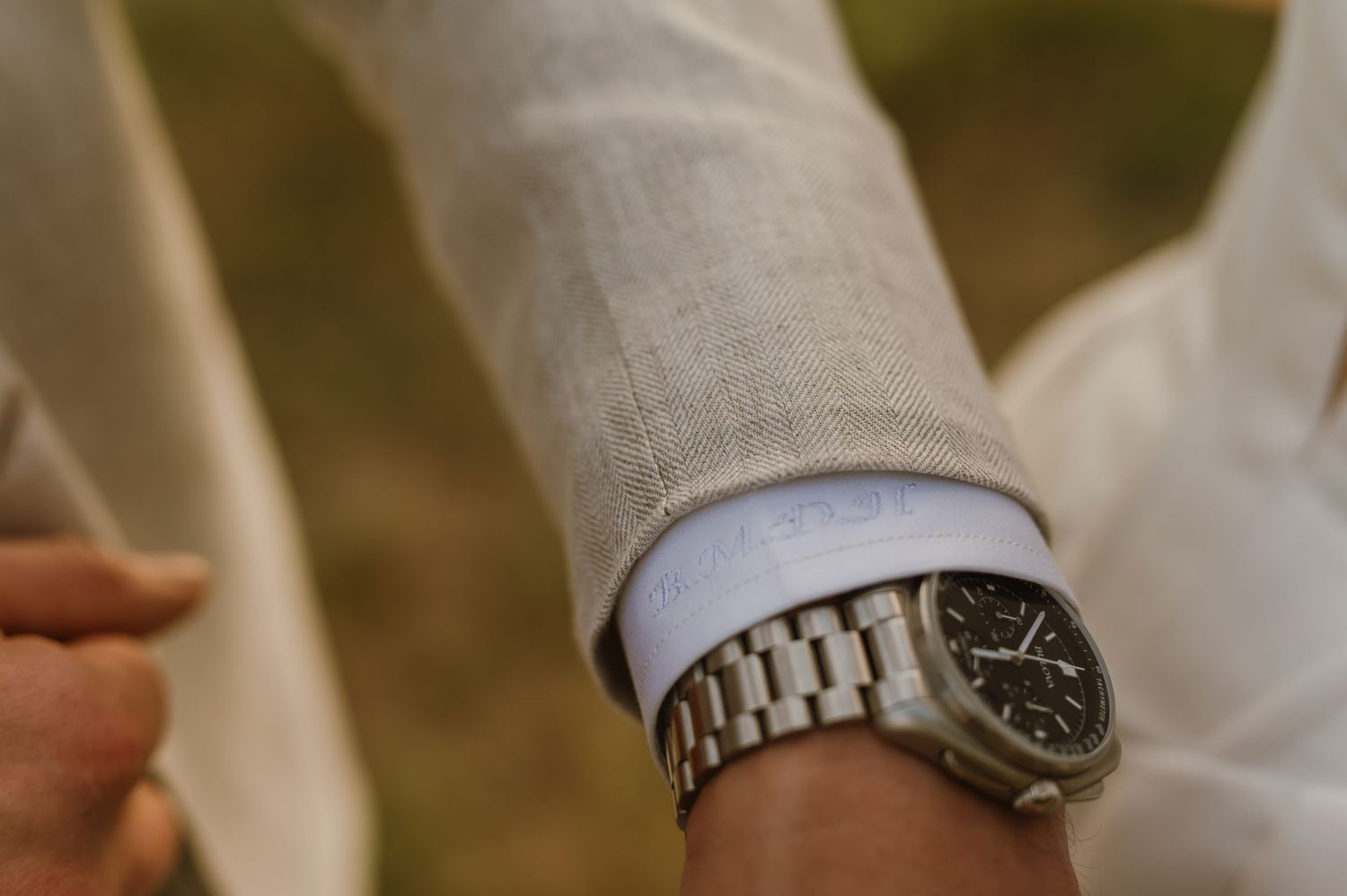 Silver wristwatch with metal band shown in detail during an outdoor wedding celebration.