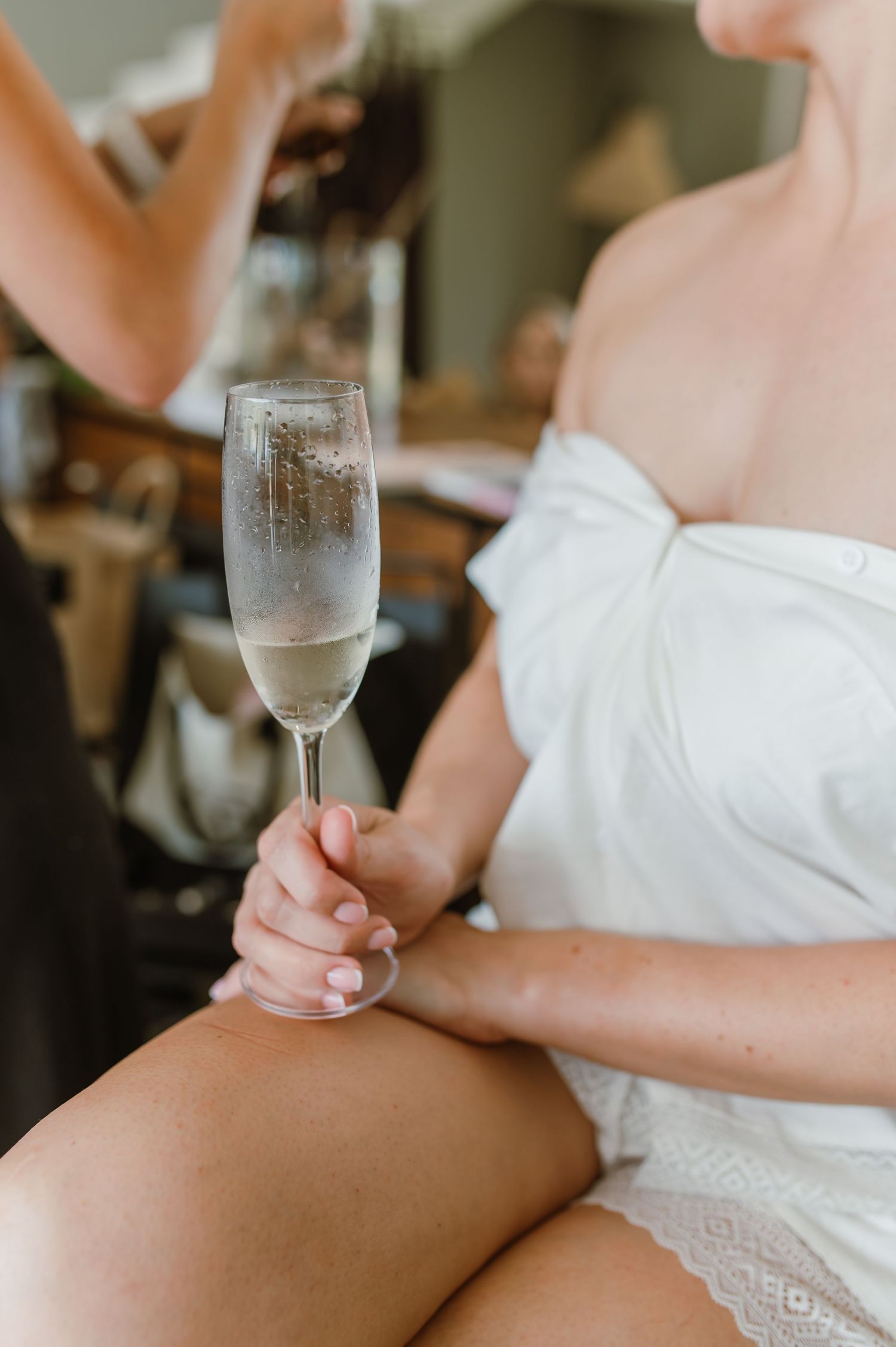 A hand holding a champagne flute while wearing a white robe or dress in an indoor setting.