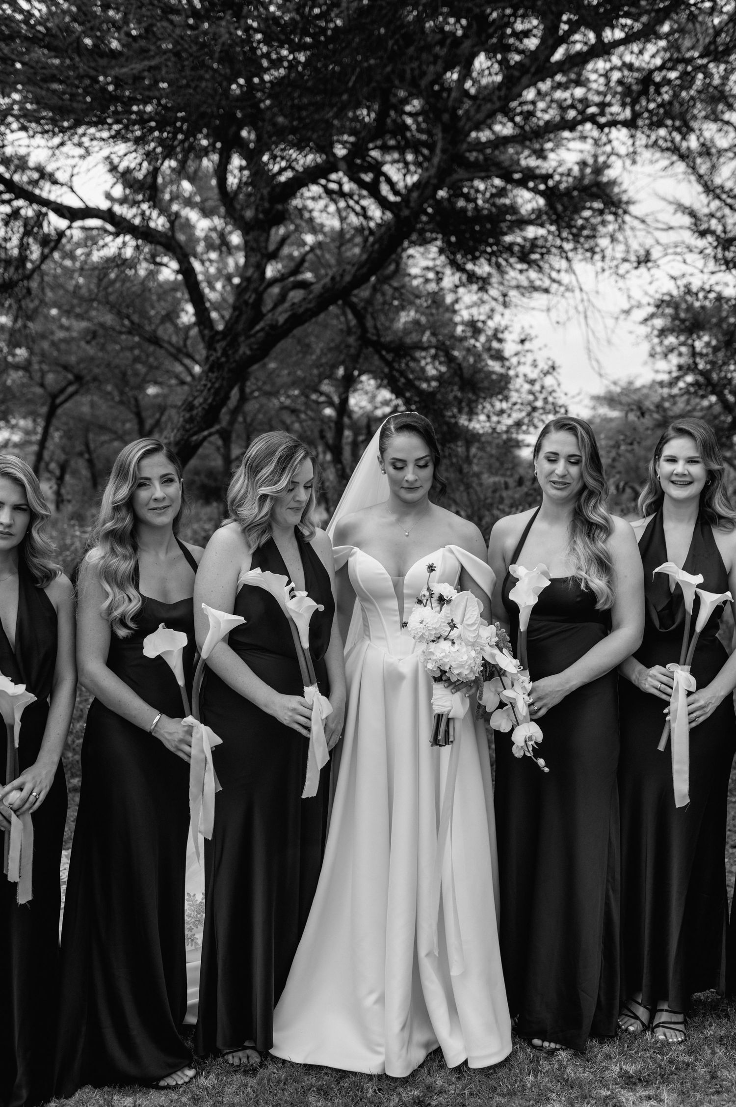 Black and white wedding photo showing a bridal party in contrasting white and black dresses holding bouquets outdoors.