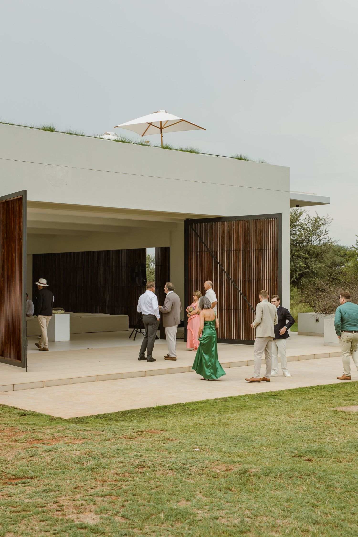 Modern minimalist venue with white walls and wooden panels hosting an outdoor gathering on a grassy lawn.