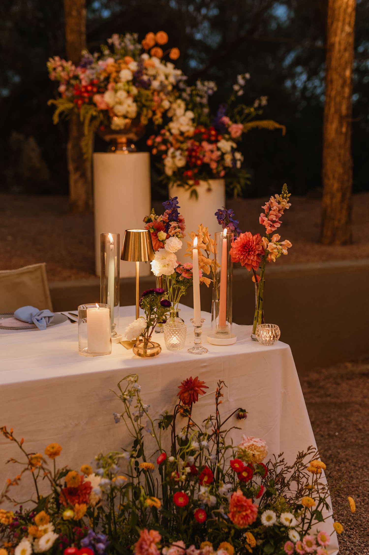 Elegant wedding sweetheart table with colorful floral arrangements, candles, and warm evening lighting.