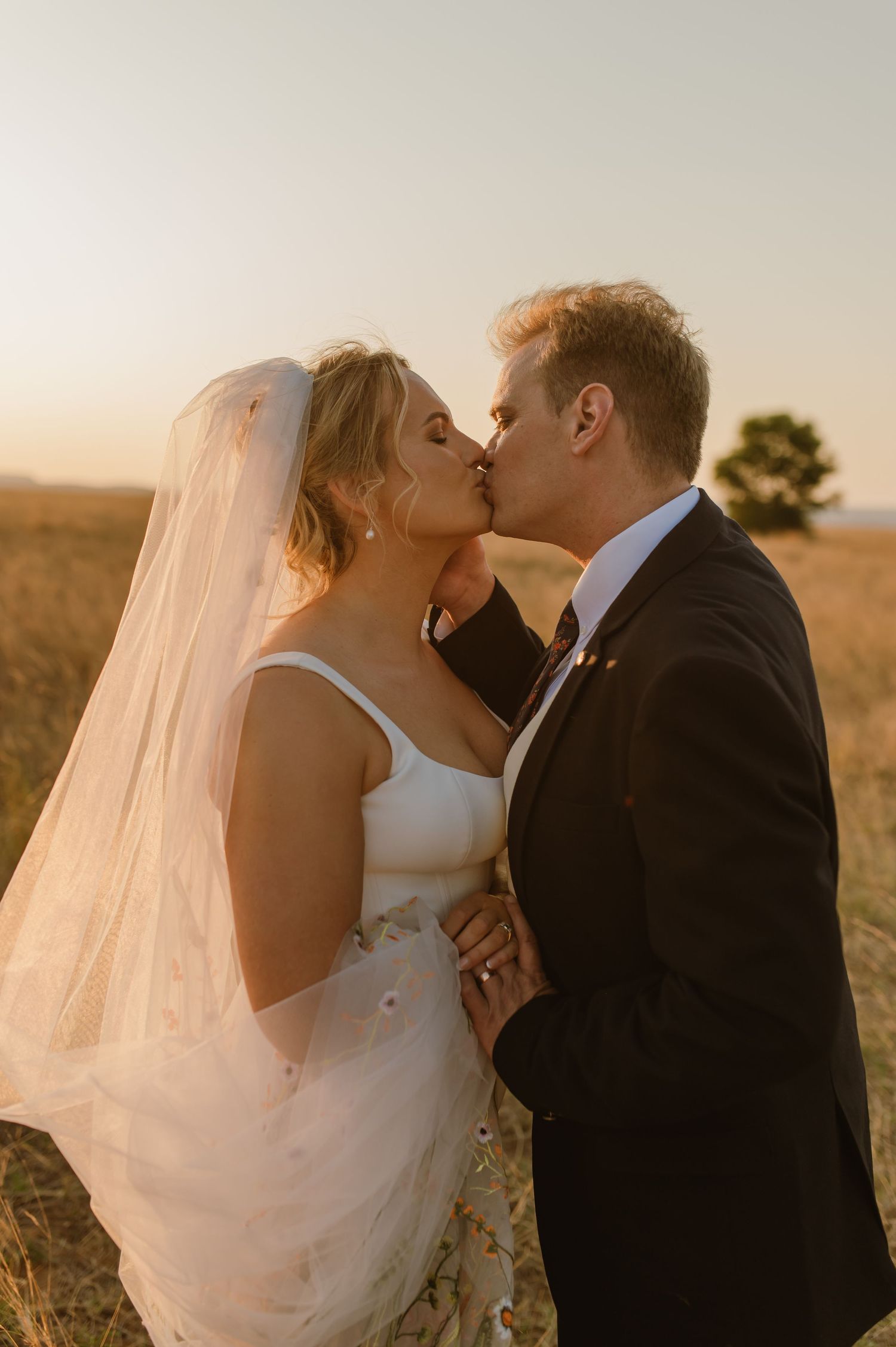 Intimate wedding moment captured in golden field during sunset.