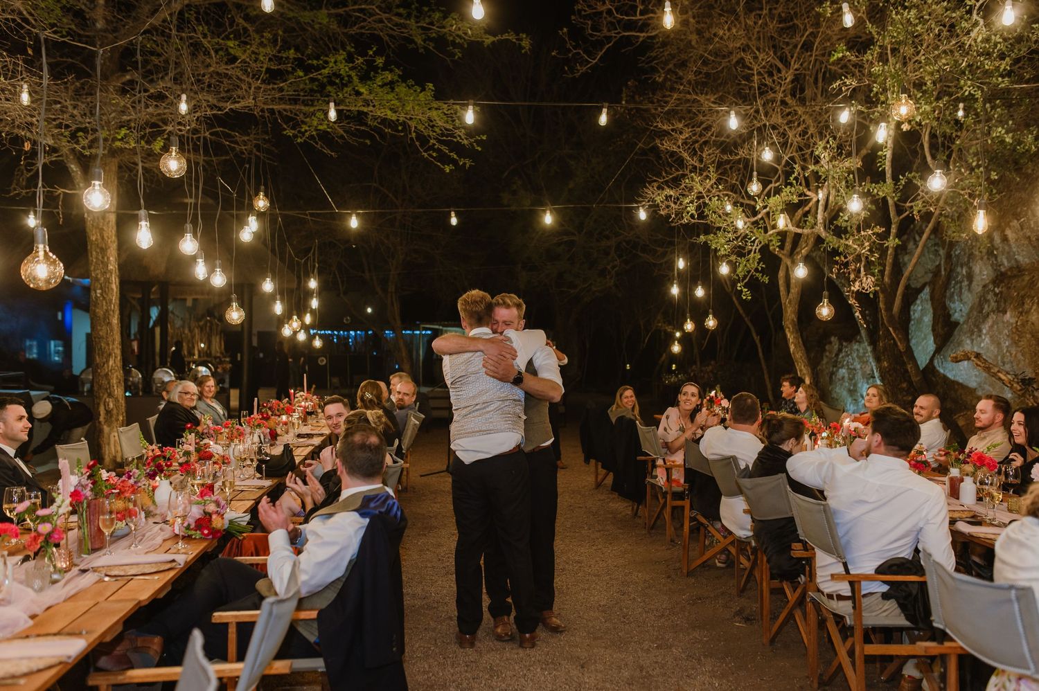 Festive outdoor celebration with string lights illuminating rows of dining tables at night.