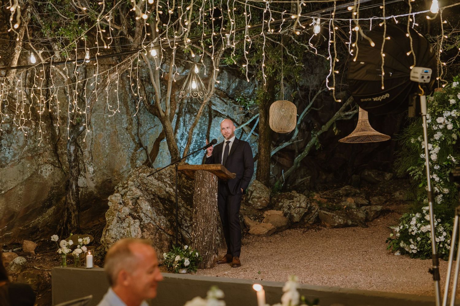 Rustic outdoor wedding venue decorated with cascading fairy lights and natural greenery.