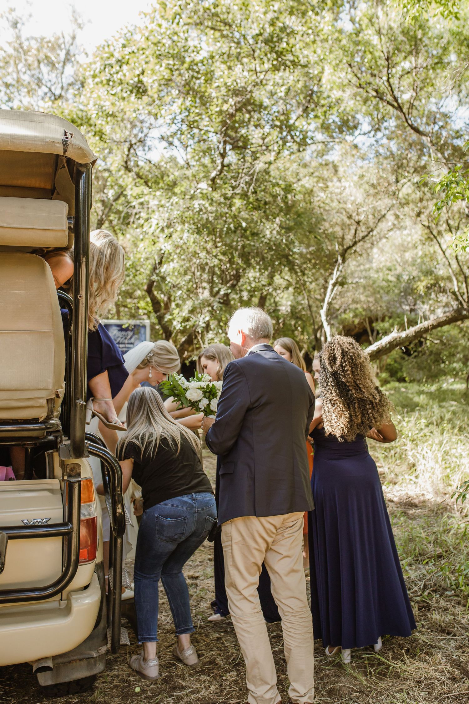 Wedding guests gather near parked vehicles at an outdoor venue.
