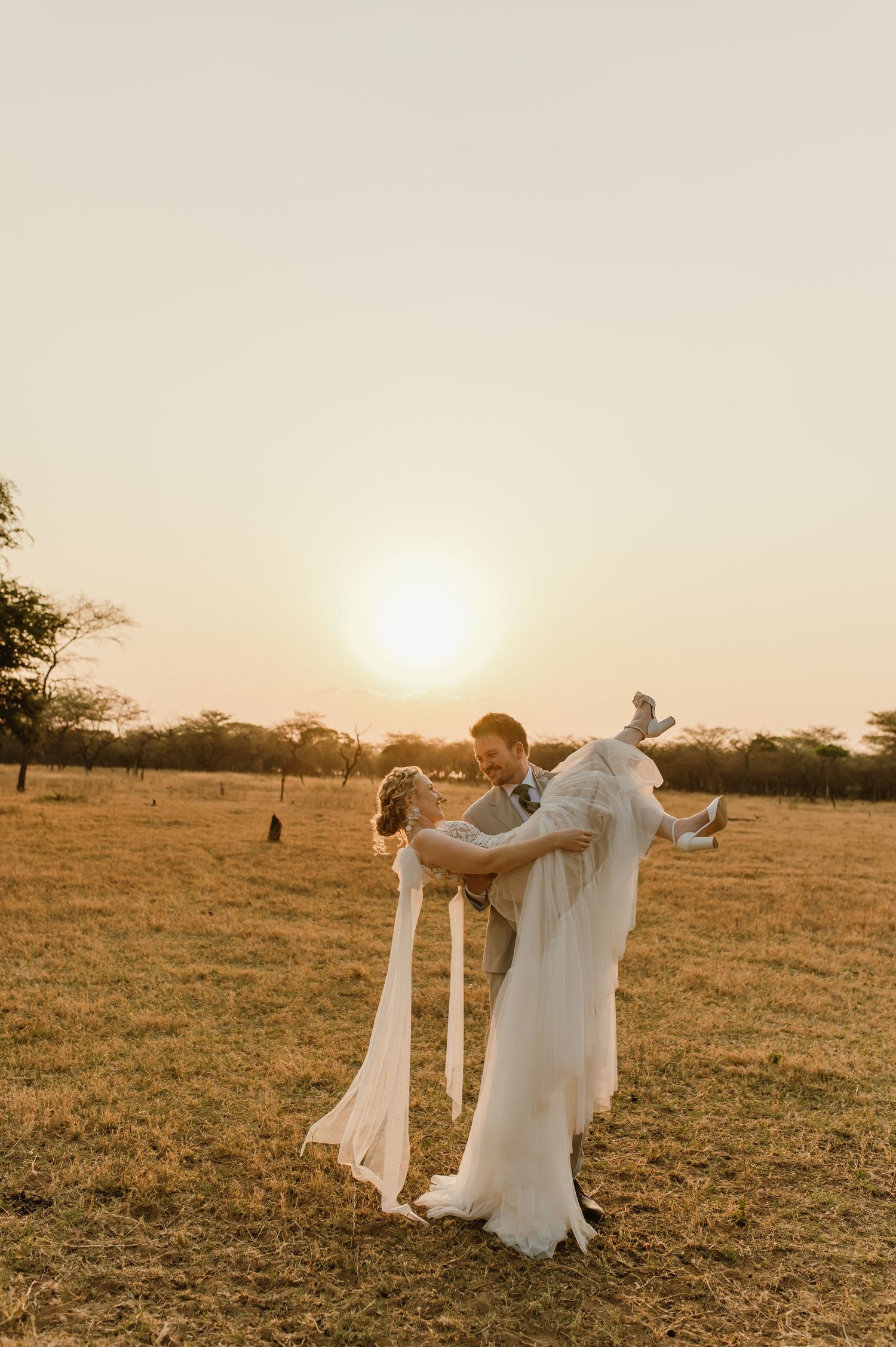 Newlyweds dance together in an African savanna during a magical sunset moment.