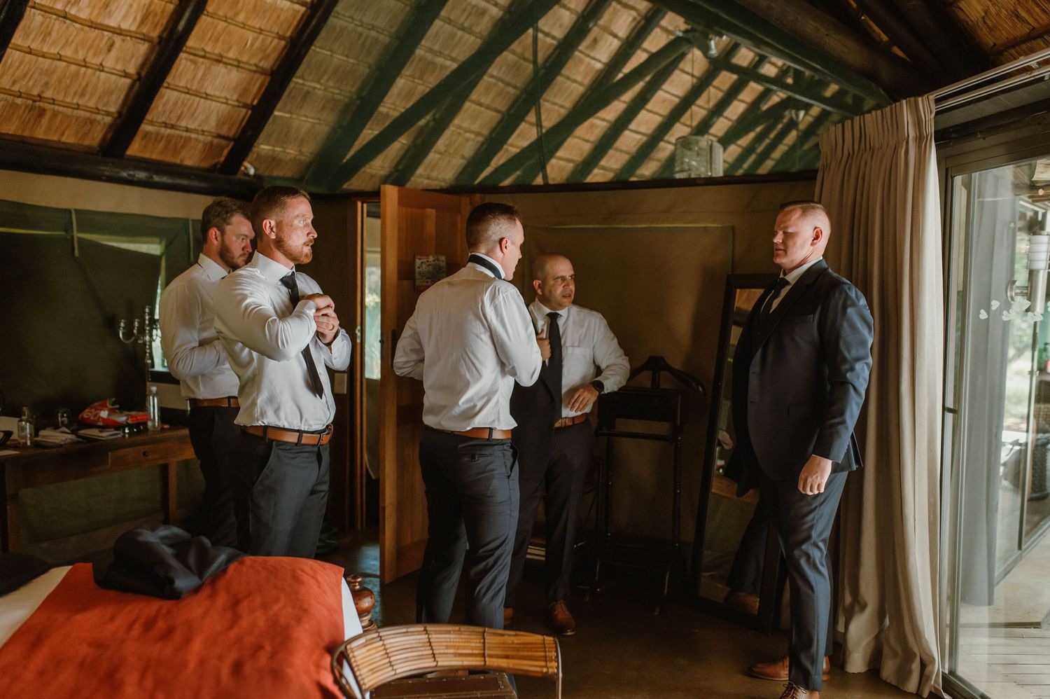 Groomsmen preparing for wedding ceremony in a wooden cabin with natural lighting.