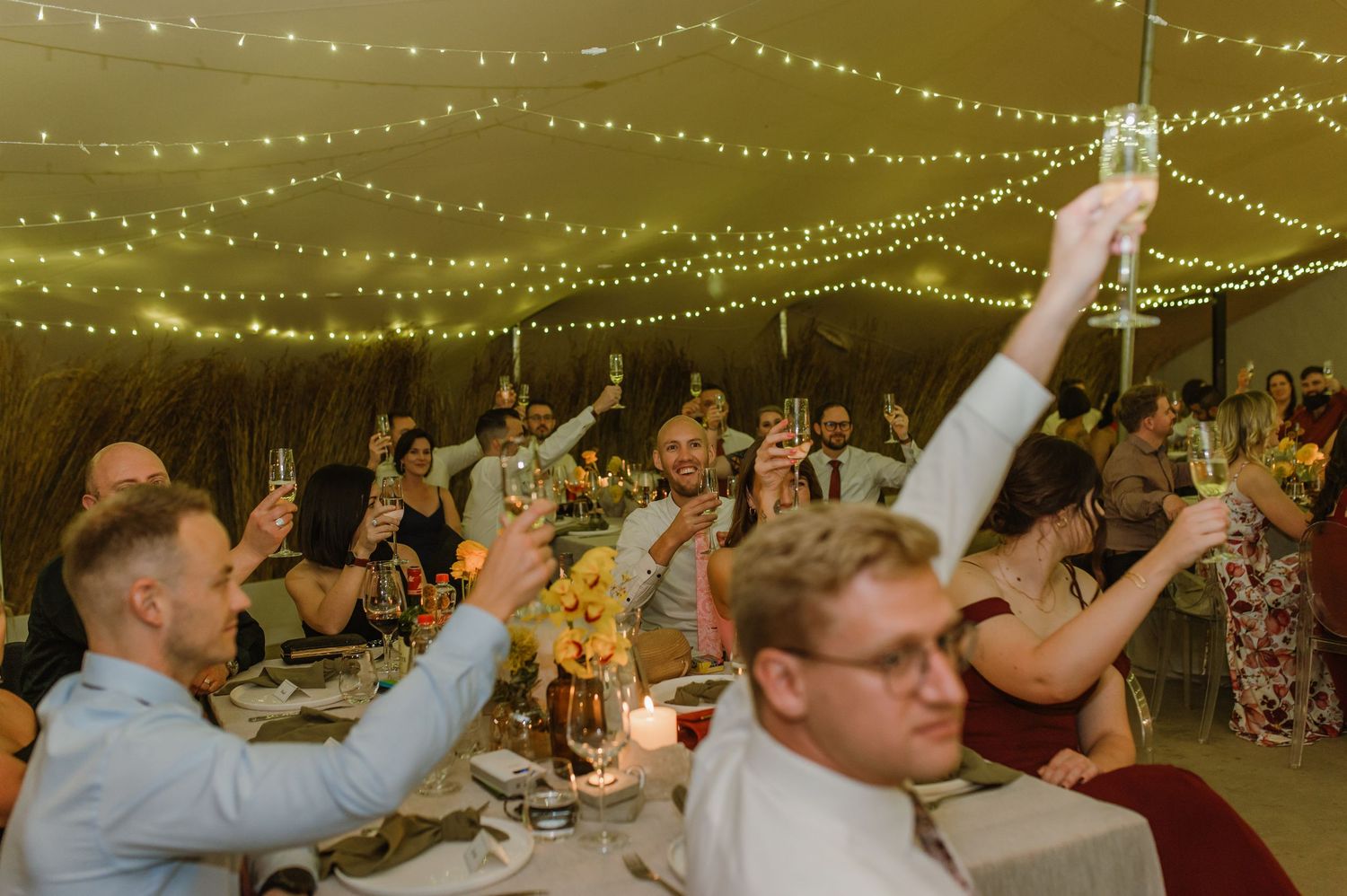 Wedding guests celebrate with raised arms under string lights at reception.