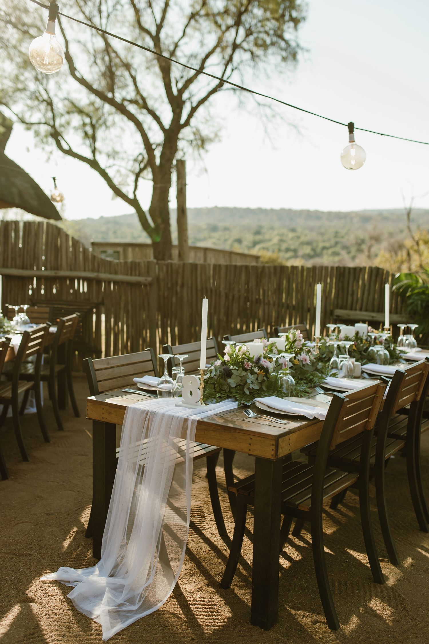 Wedding table setup with flowing white fabric runner and elegant place settings in outdoor desert setting.