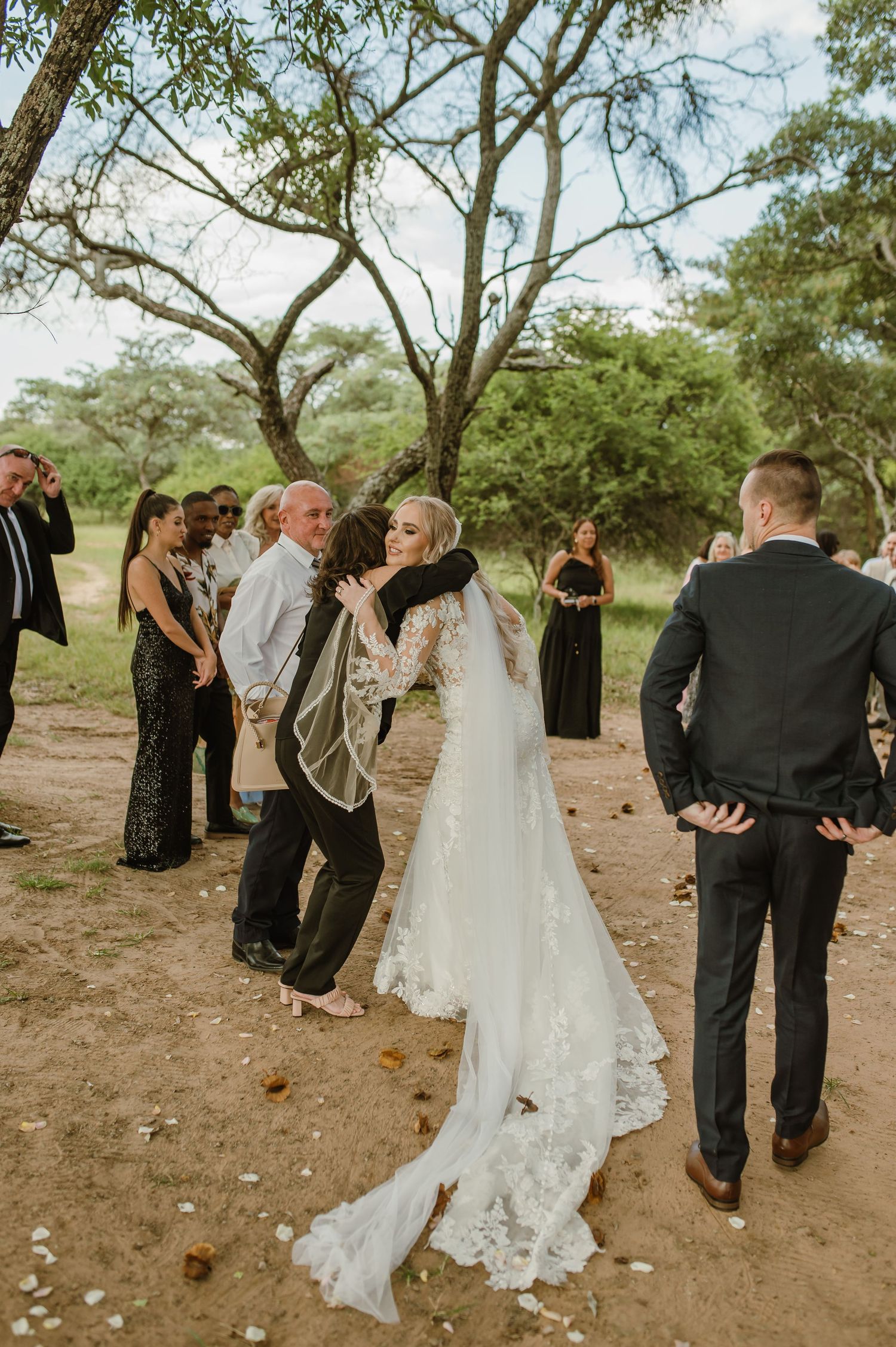 Wedding celebration with guests mingling on natural dirt path under trees.
