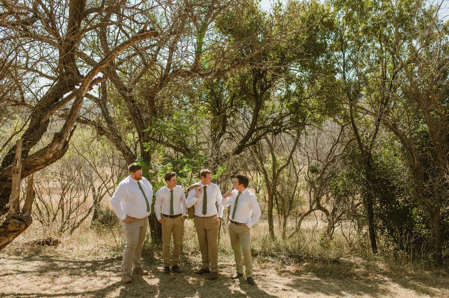 Wedding party poses among trees in natural African bush setting.