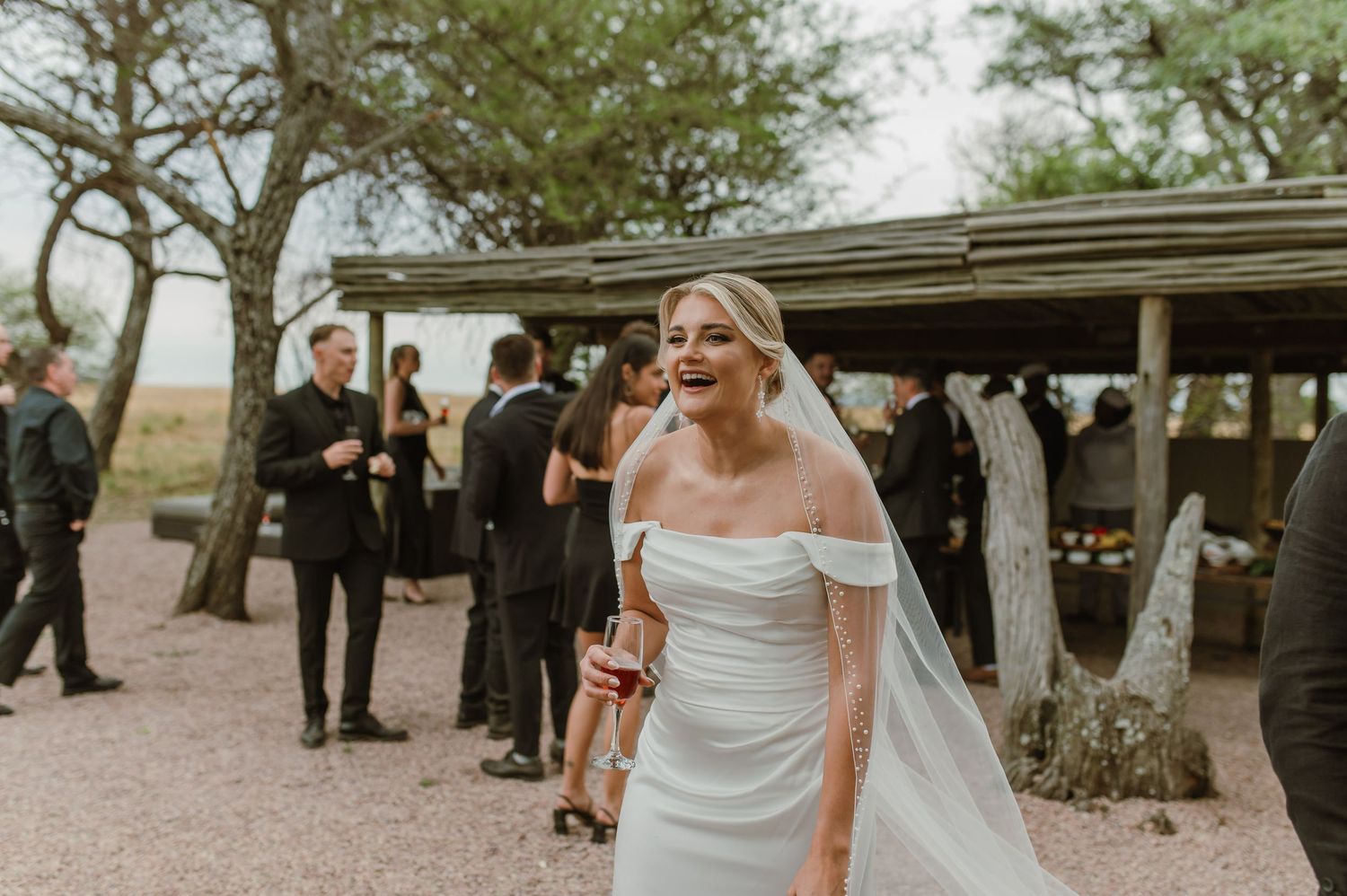 Wedding guests gathered outdoors under trees at an elegant venue.