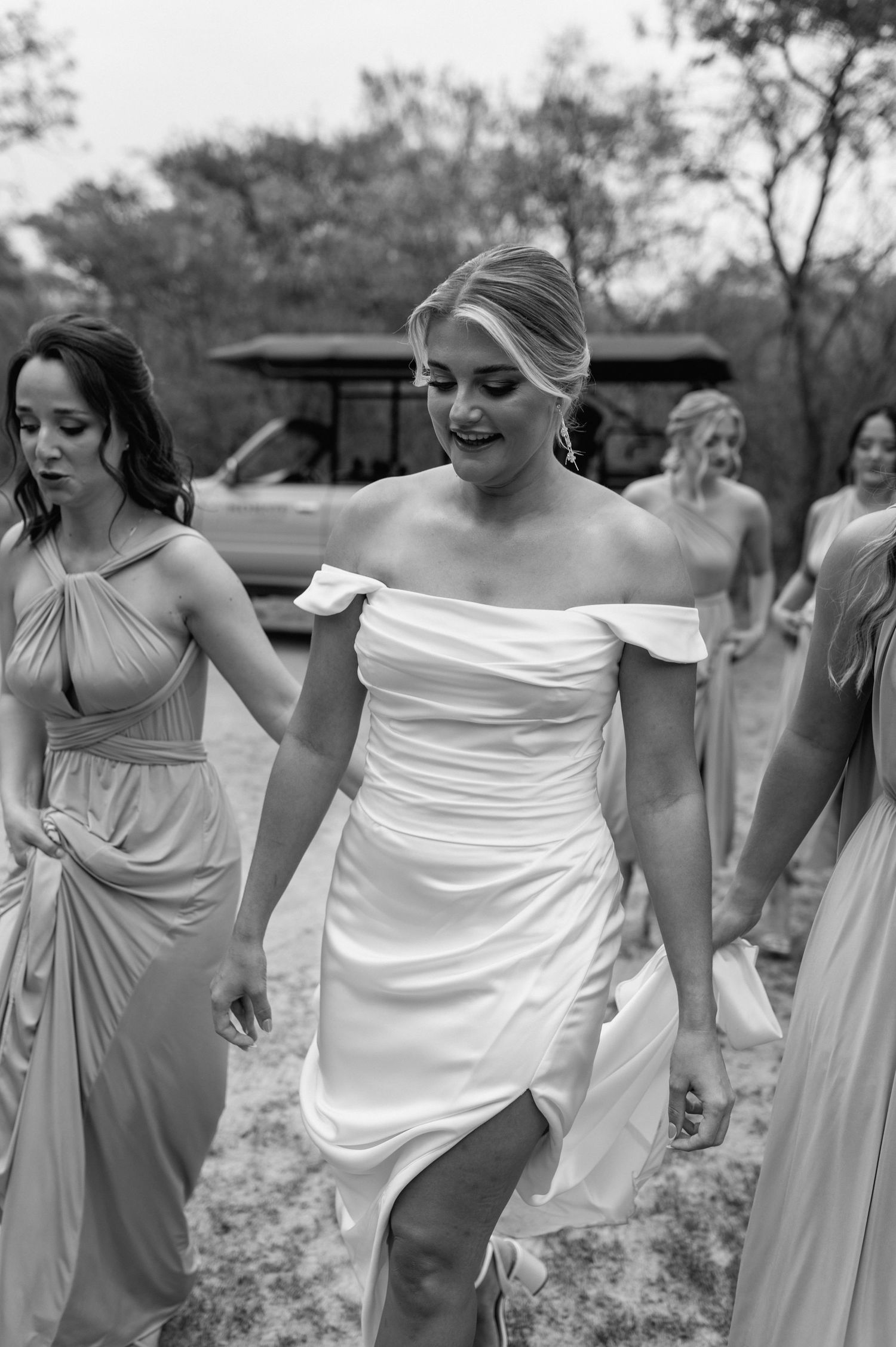 Black and white photo of bridal party walking in flowing dresses outdoors.