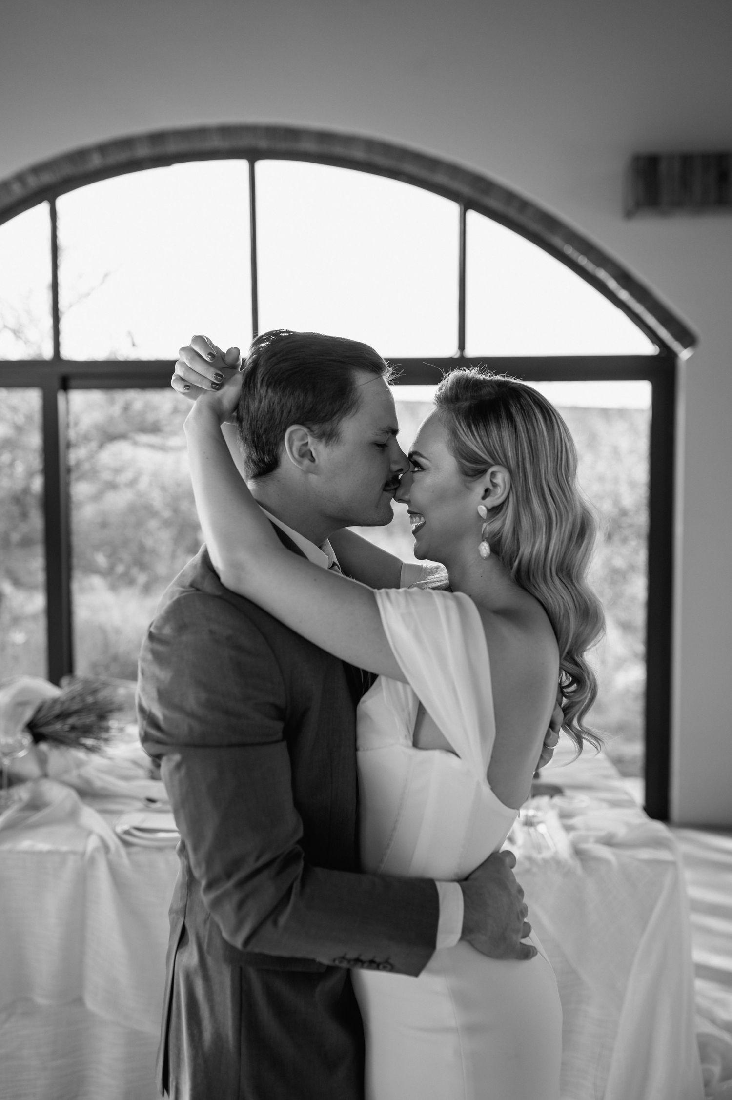 Romantic black and white dance pose in an elegant venue with arched windows.