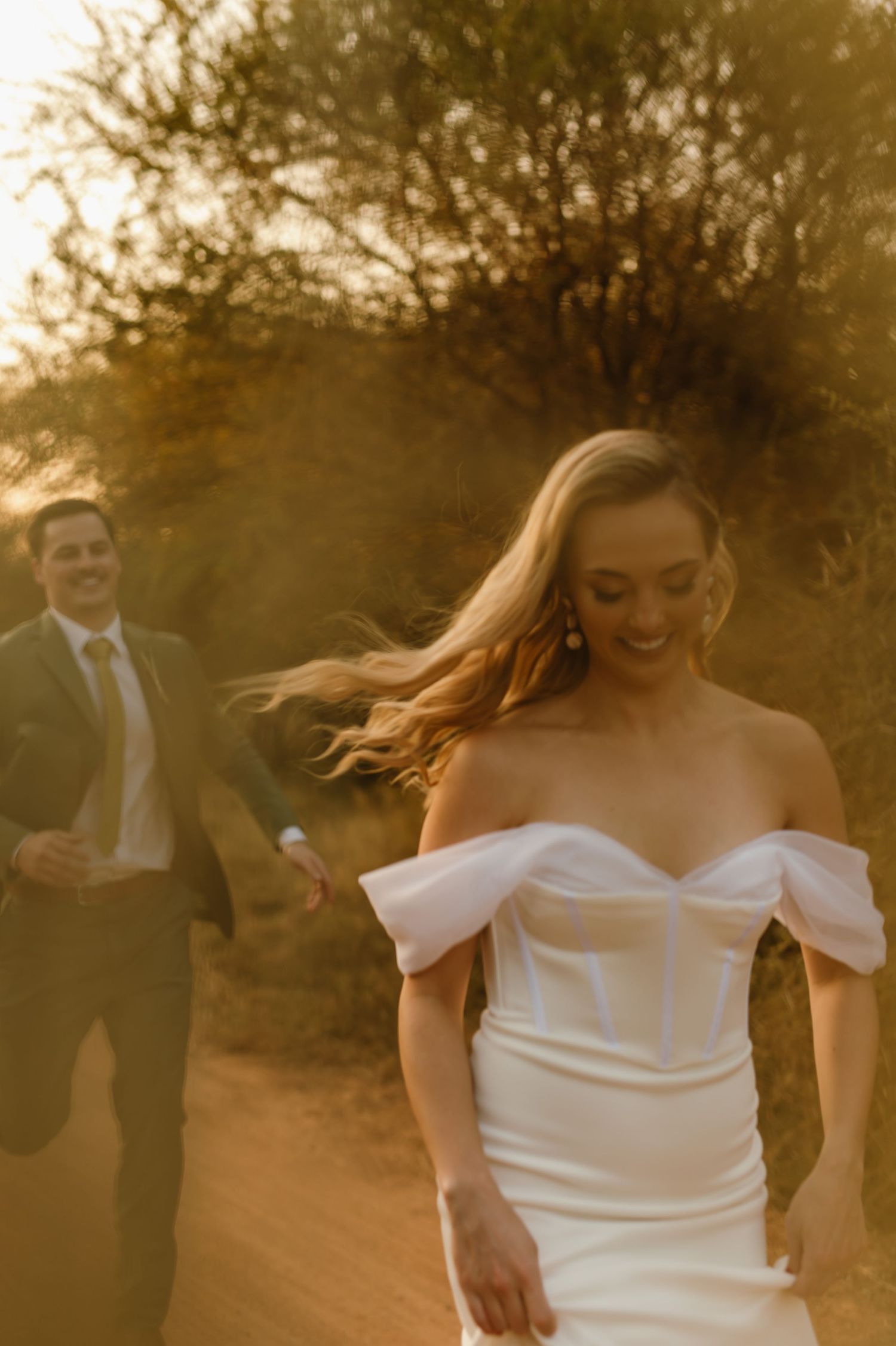 Bride in off-shoulder dress twirling on a desert path with golden sunset lighting.